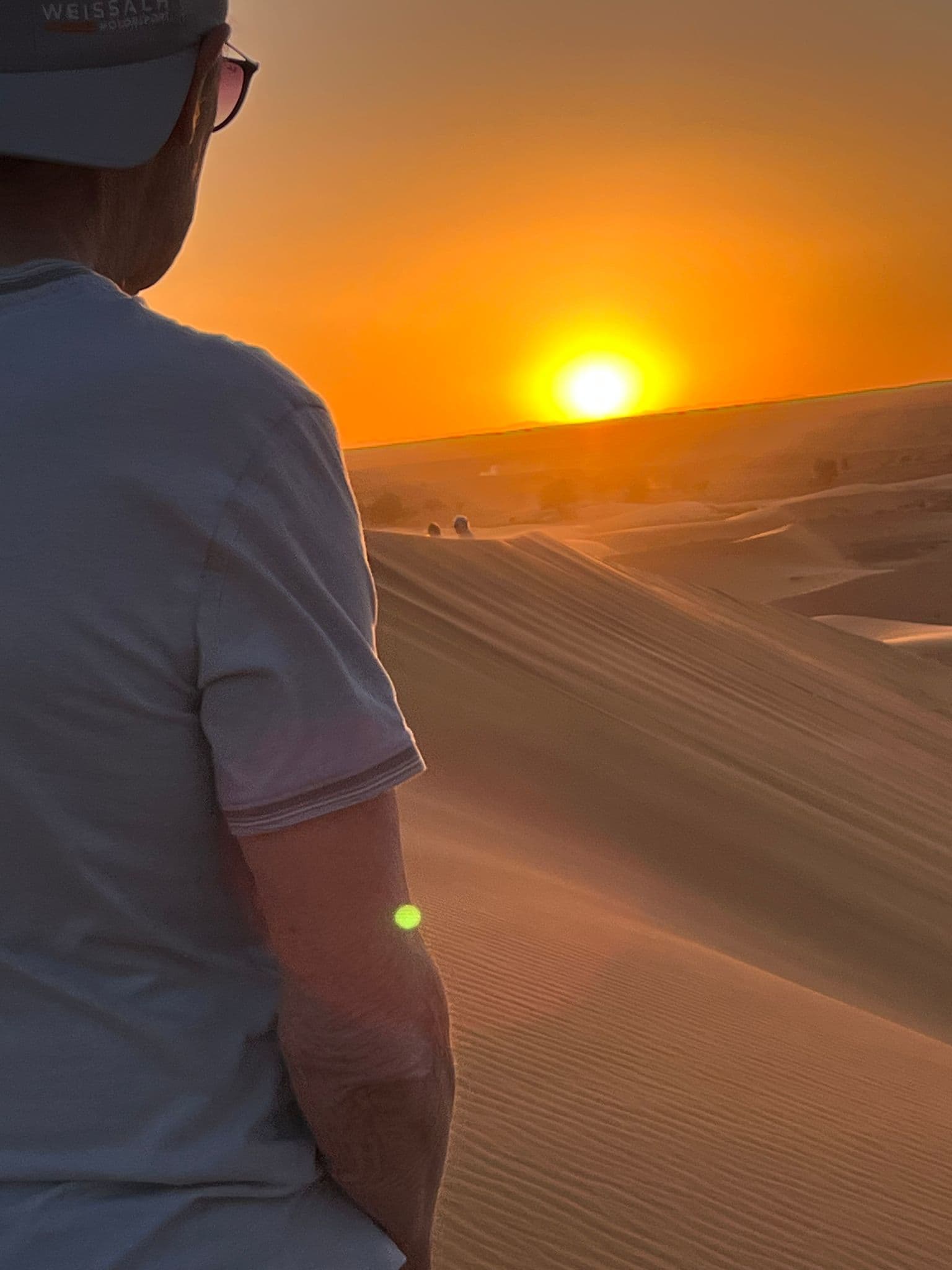 Sunset over sand dunes in the Sahara Desert, Morocco, with a traveler standing on a dune watching the sun.