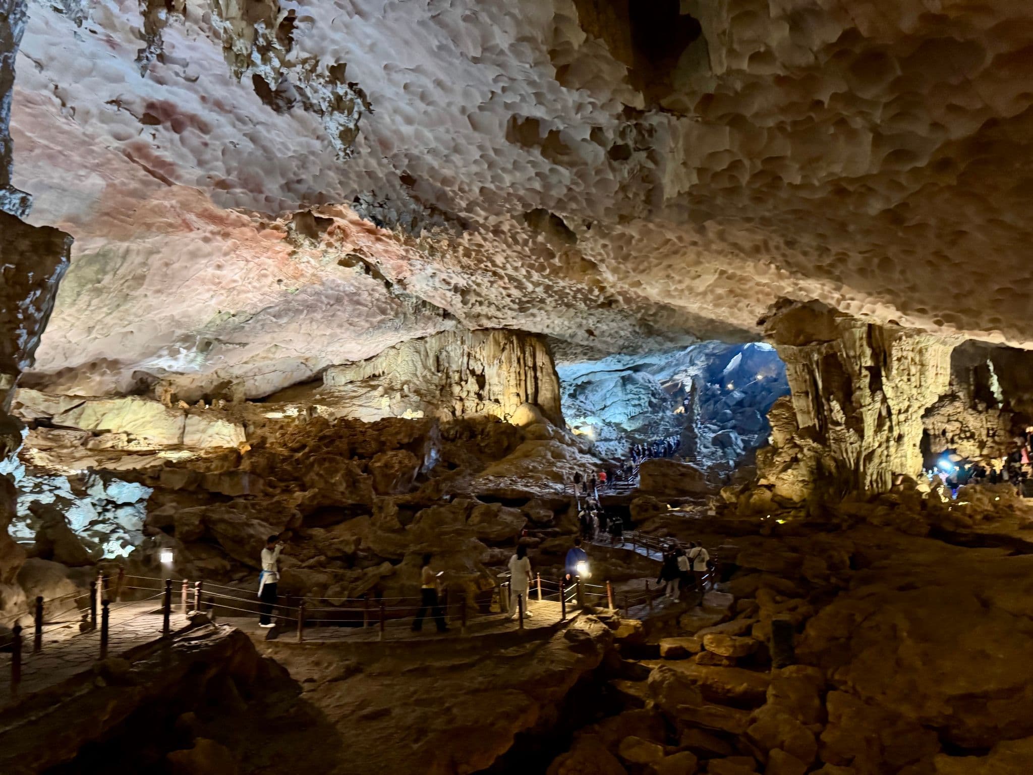 Large illuminated limestone cave interior with visitors walking on a raised path in Ha Long Bay, Vietnam.