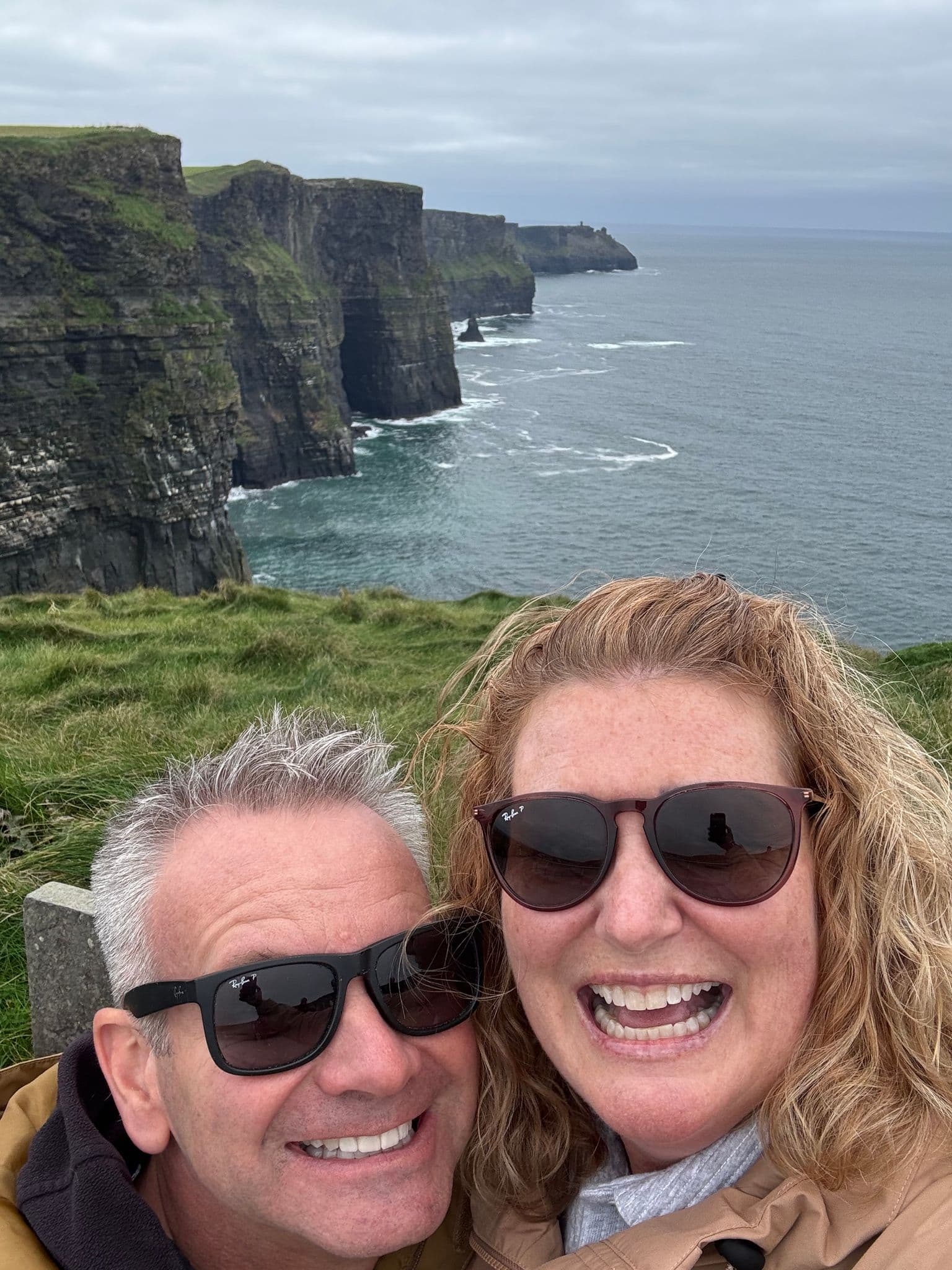 Cliffs of Moher rising above the Atlantic with two travelers smiling for a selfie on a tour, County Clare, Ireland.