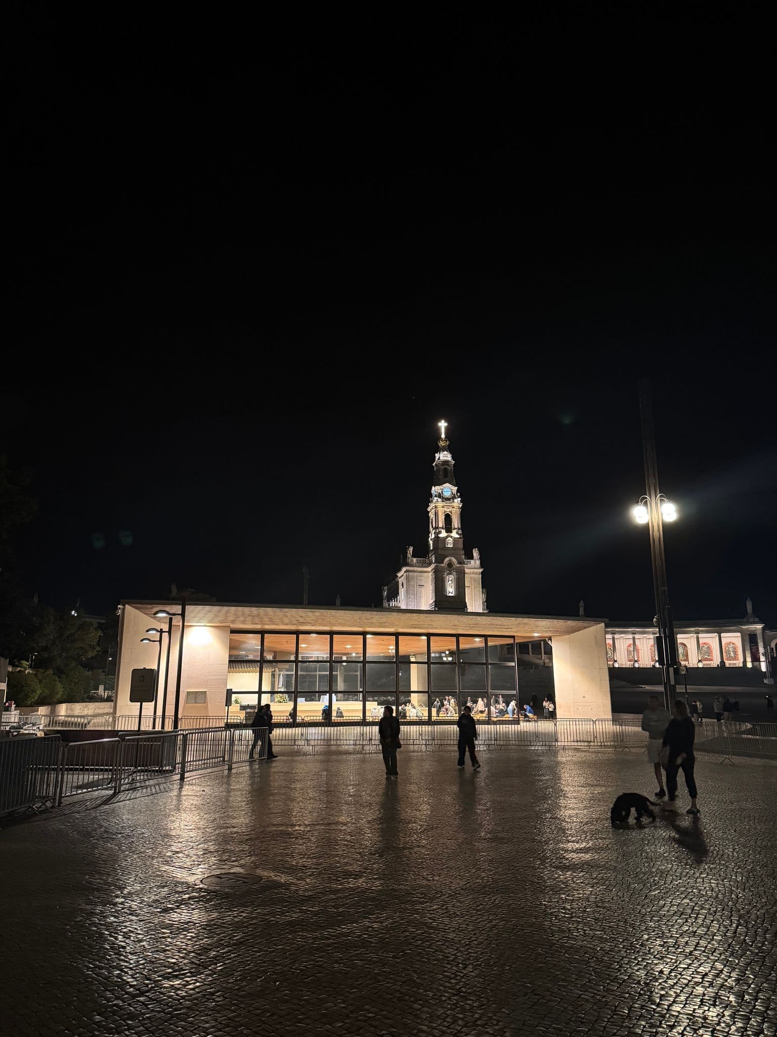 Sanctuary of Our Lady of Fátima bell tower above the lit Chapel of the Apparitions with people praying inside, Fátima, Portugal.