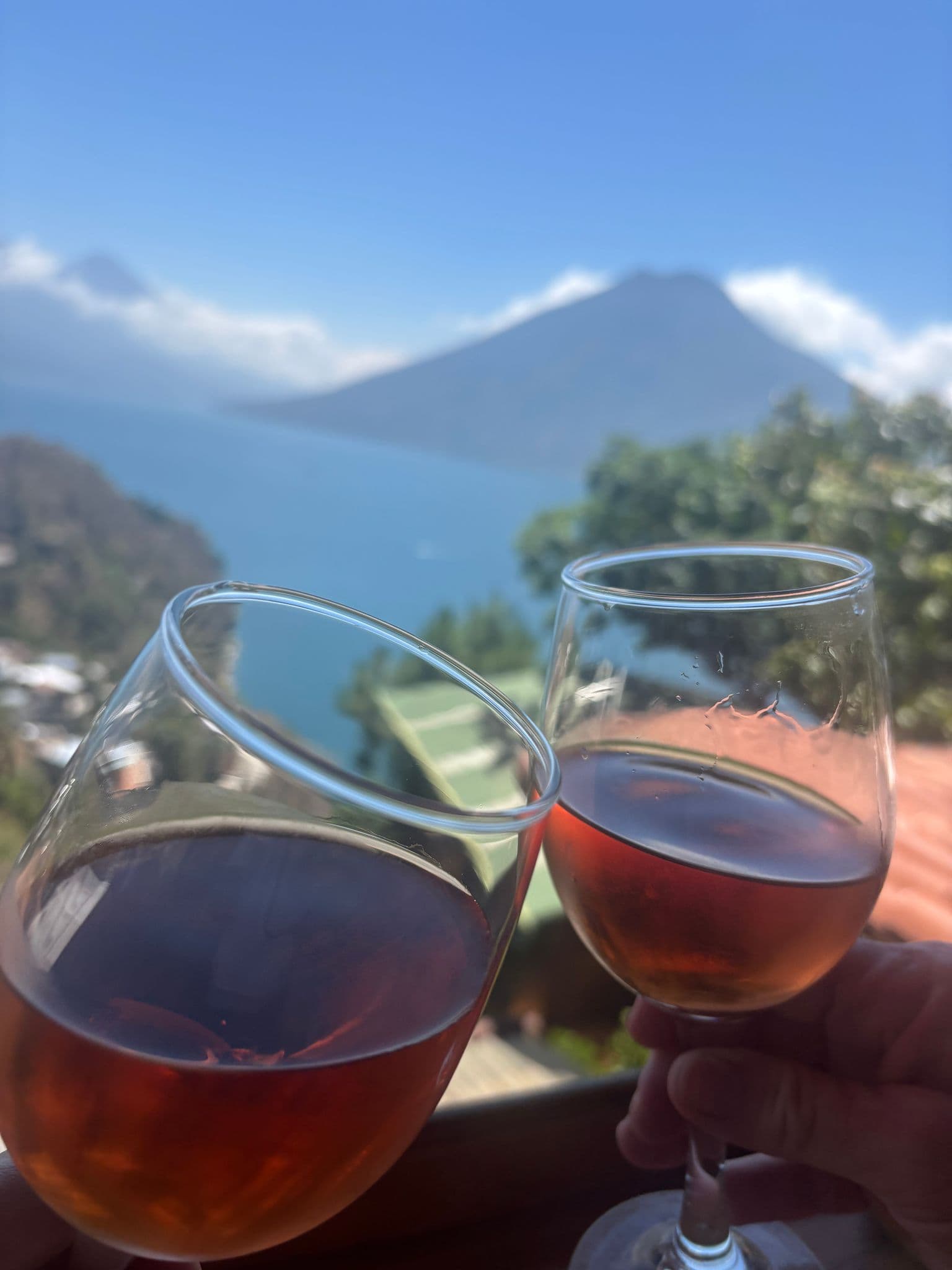 Lake Atitlán with Volcán San Pedro in the distance, two glasses of rosé wine clinking on a balcony in San Marcos La Laguna, Guatemala