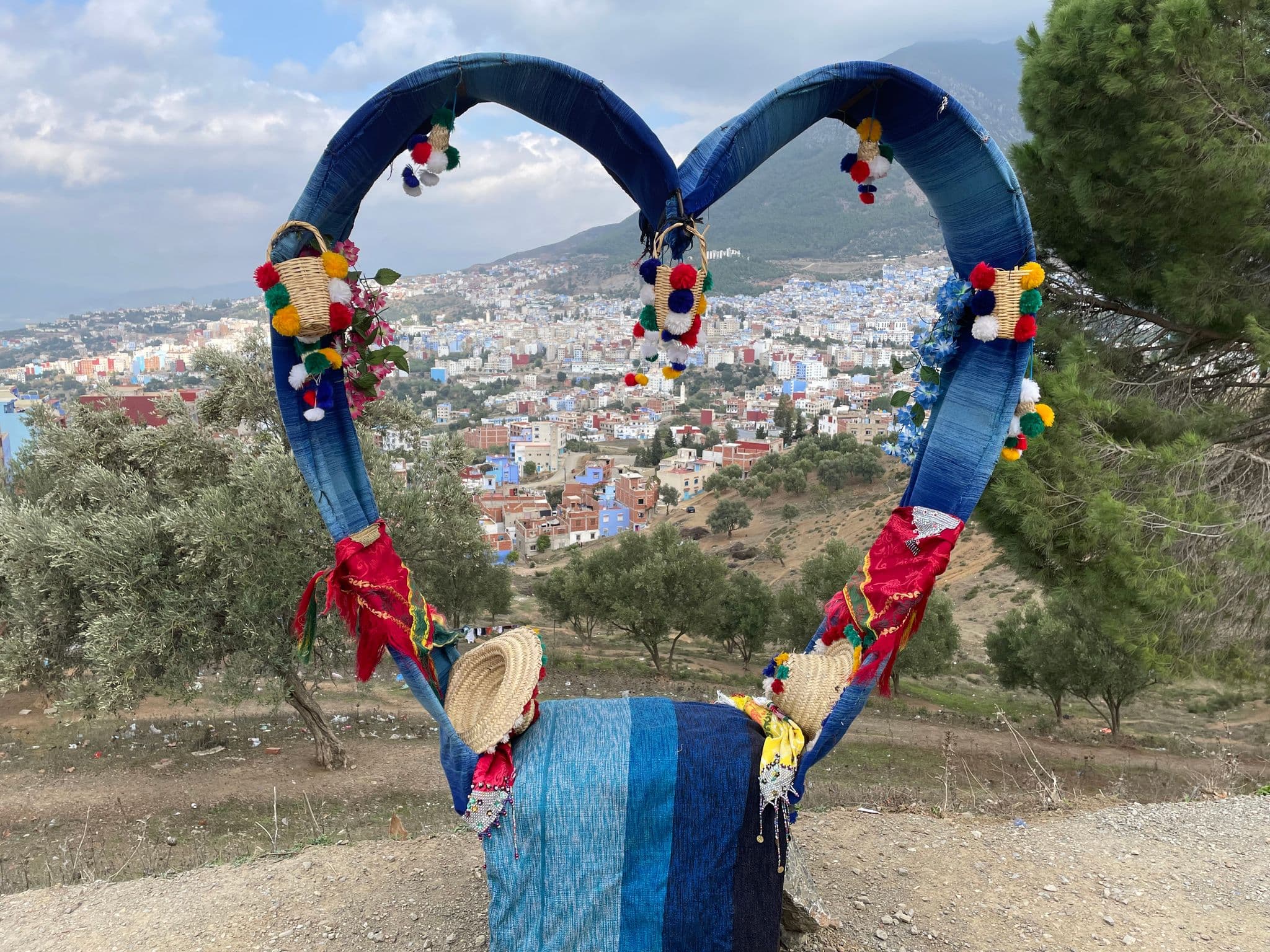 Decorative heart-shaped fabric frame overlooking the blue-painted buildings of Chefchaouen, Morocco, from a hillside.
