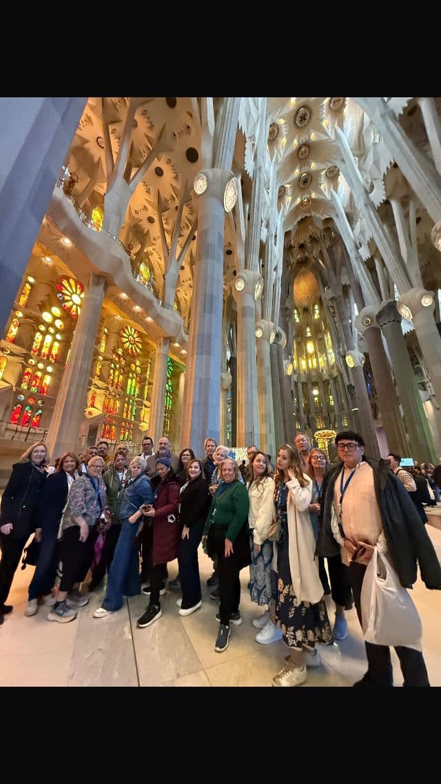 Interior of the Sagrada Família in Barcelona, Spain, with a tour group posing beneath colorful stained-glass windows and tall columns.