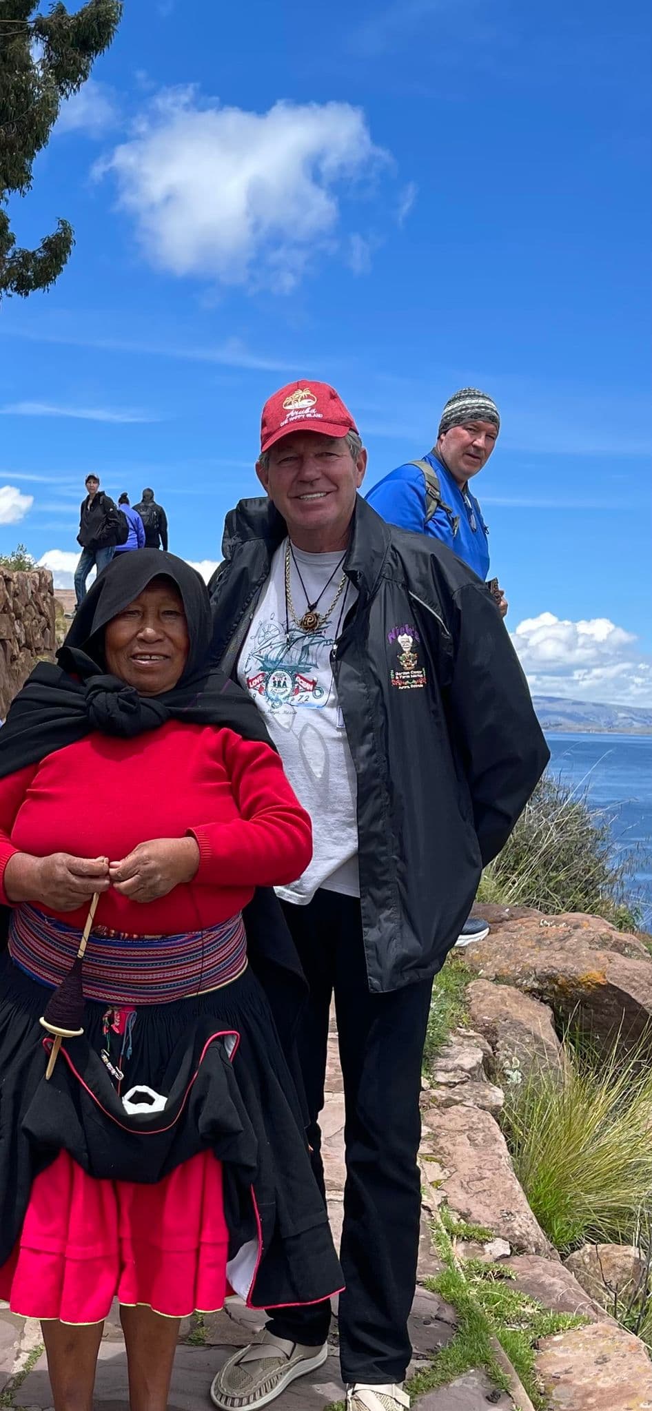 Lake Titicaca shoreline with a local woman in traditional dress and a tourist standing on a rocky path, Peru.
