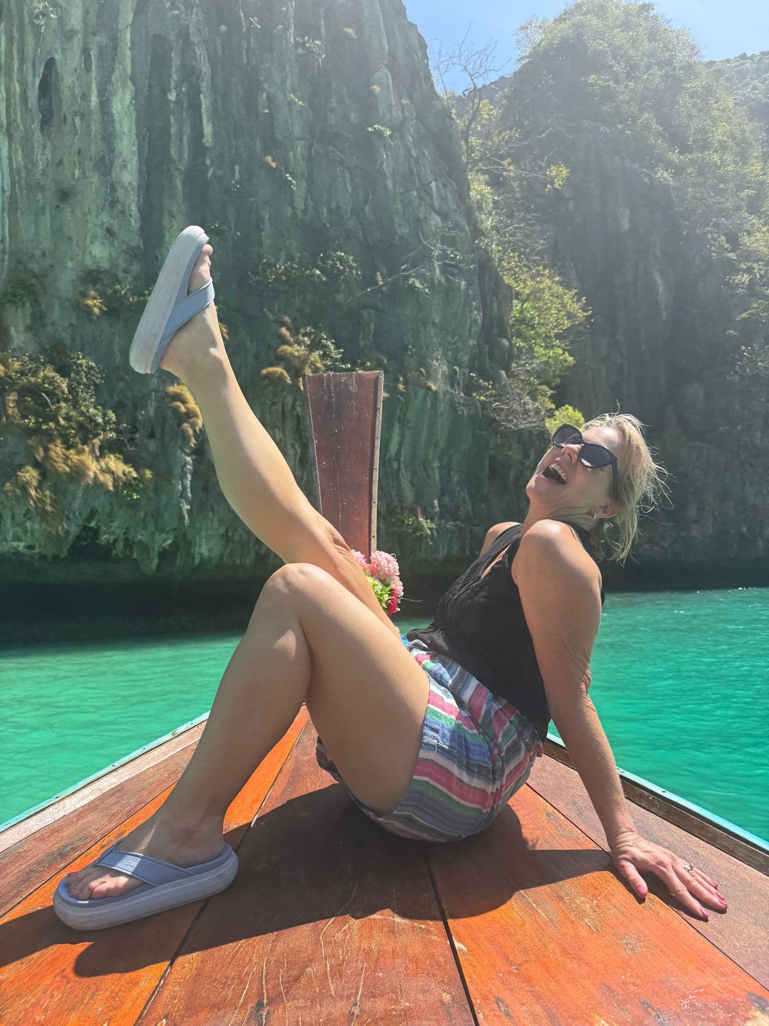 Longtail boat bow with a traveler posing on turquoise water at Phi Phi Islands, Thailand.