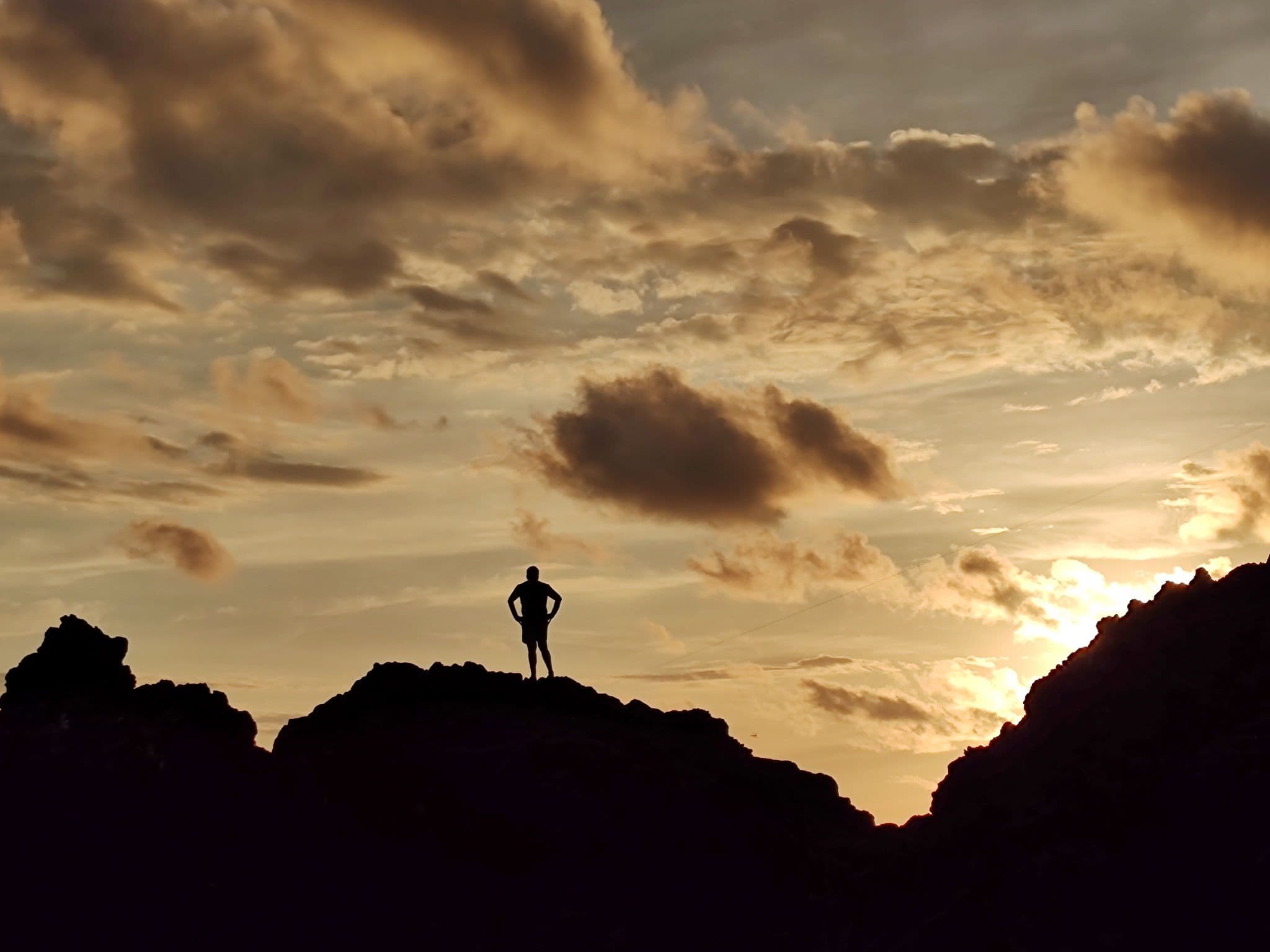 Silhouette of a person standing on rocky cliffs at sunset in Manuel Antonio National Park, Costa Rica.