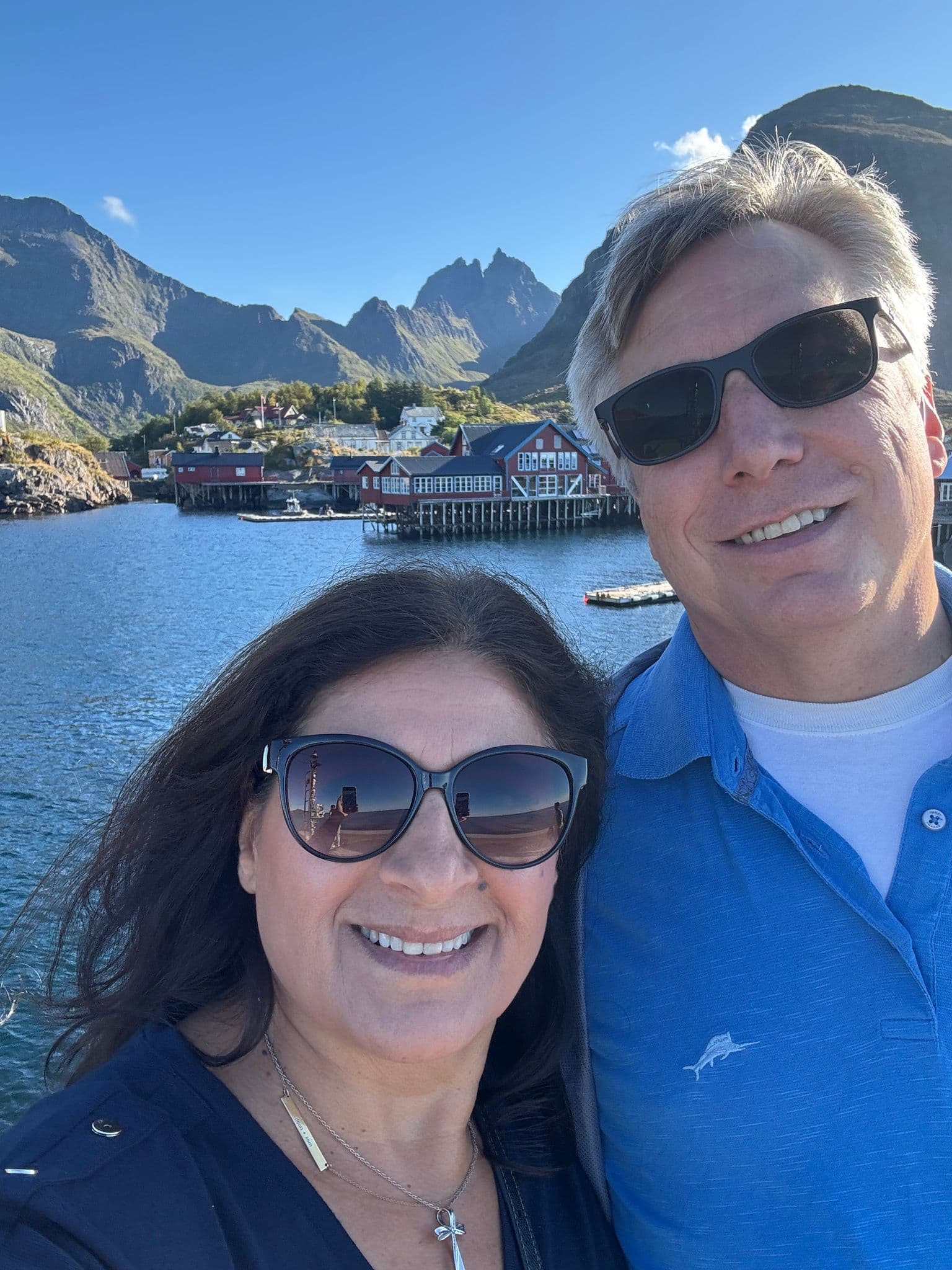 Red rorbuer houses on stilts in Reine, Lofoten, Norway with a couple taking a selfie by the water.