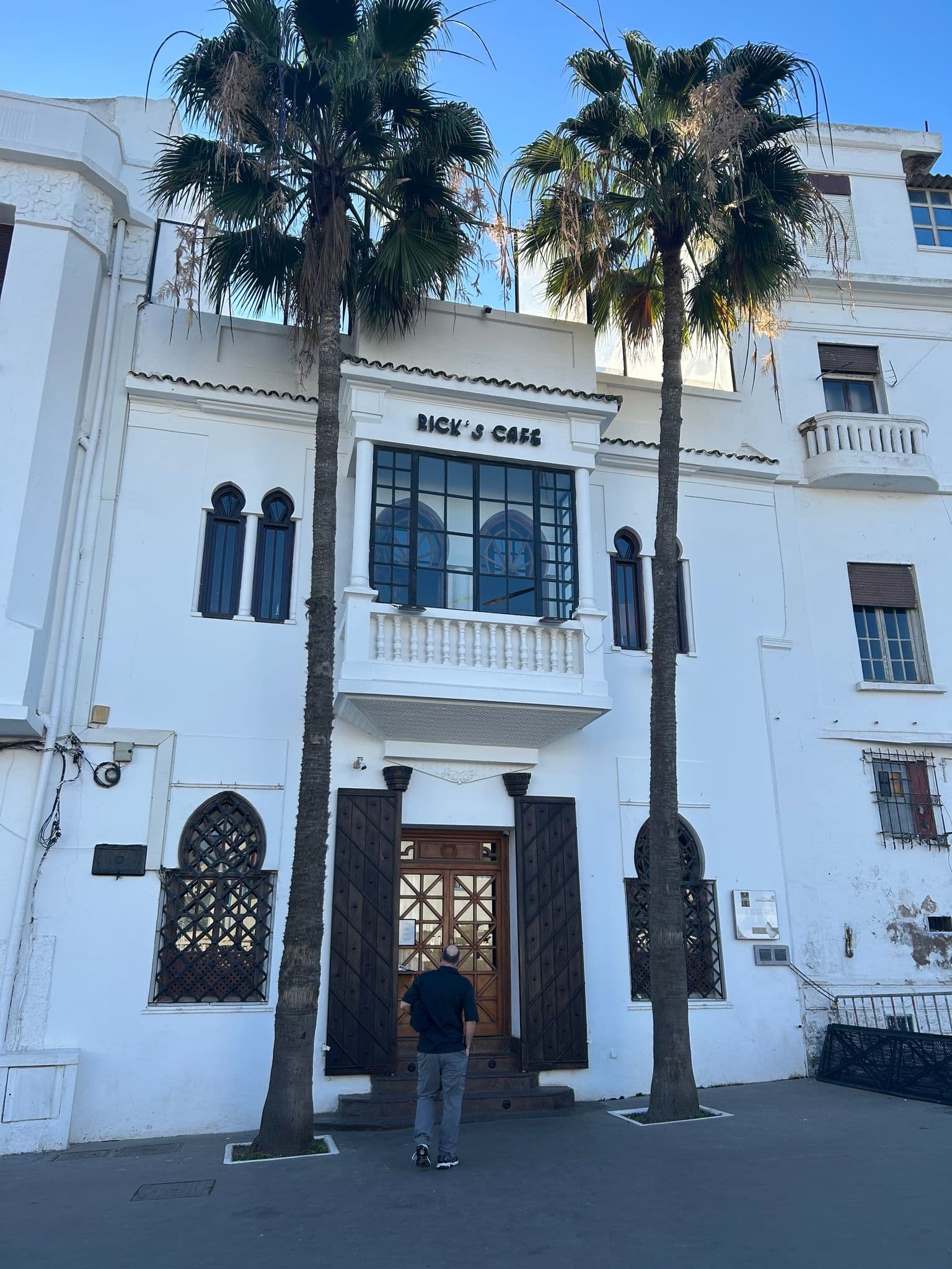 Rick's Café facade in Casablanca, Morocco with a person standing at the wooden entrance between two palm trees.