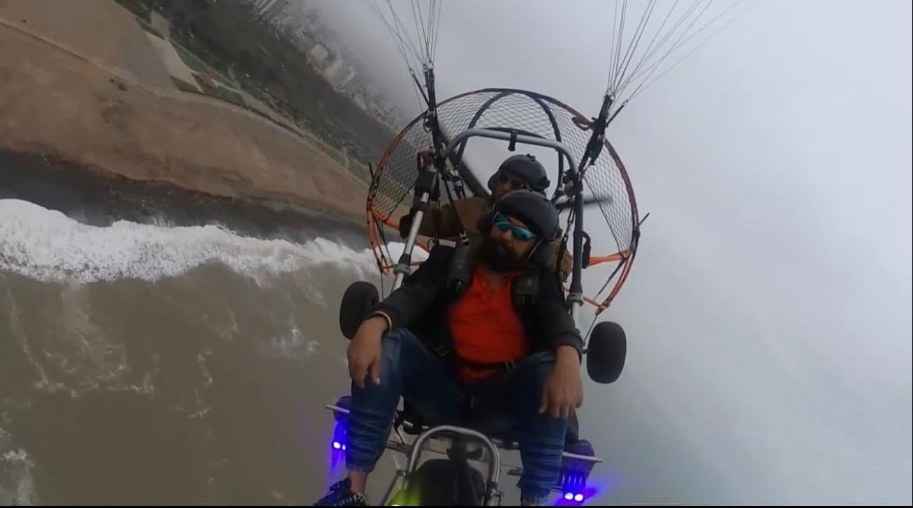 Two people in a powered paraglider flying above the Miraflores cliffs and coast in Lima, Peru.