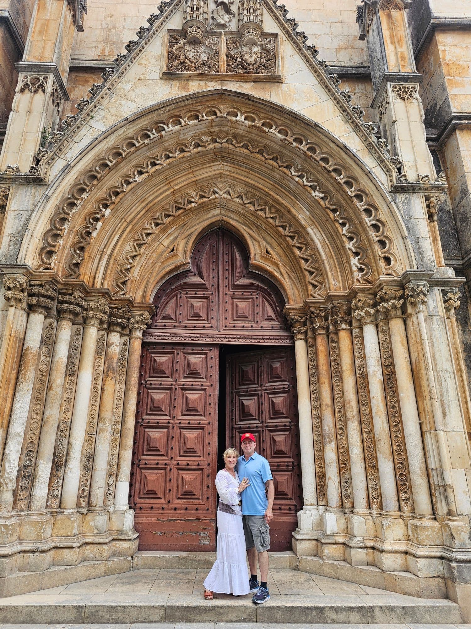 Entrance of Batalha Monastery in Batalha, Portugal with a couple standing by the ornate carved wooden doorway.