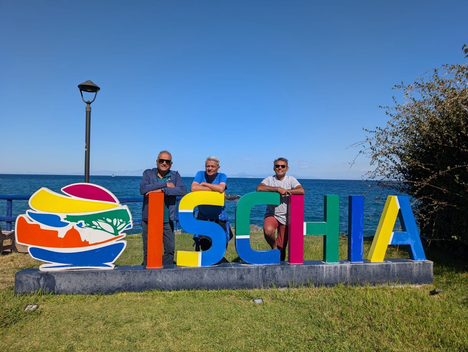 Ischia sign with three men leaning on colorful letters beside the sea on Ischia, Italy.