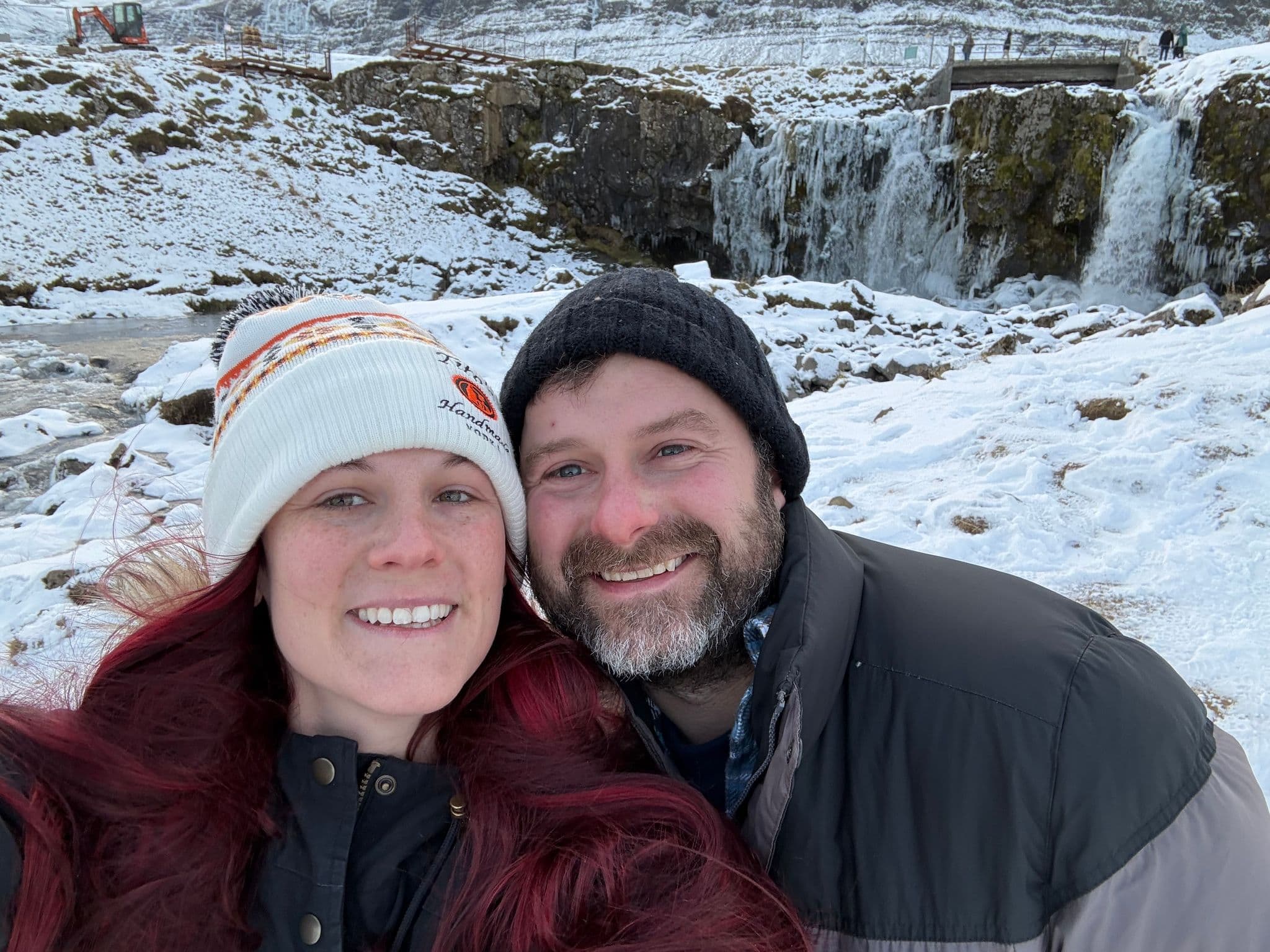 A couple taking a selfie in front of a snow-covered waterfall and frozen river in Iceland