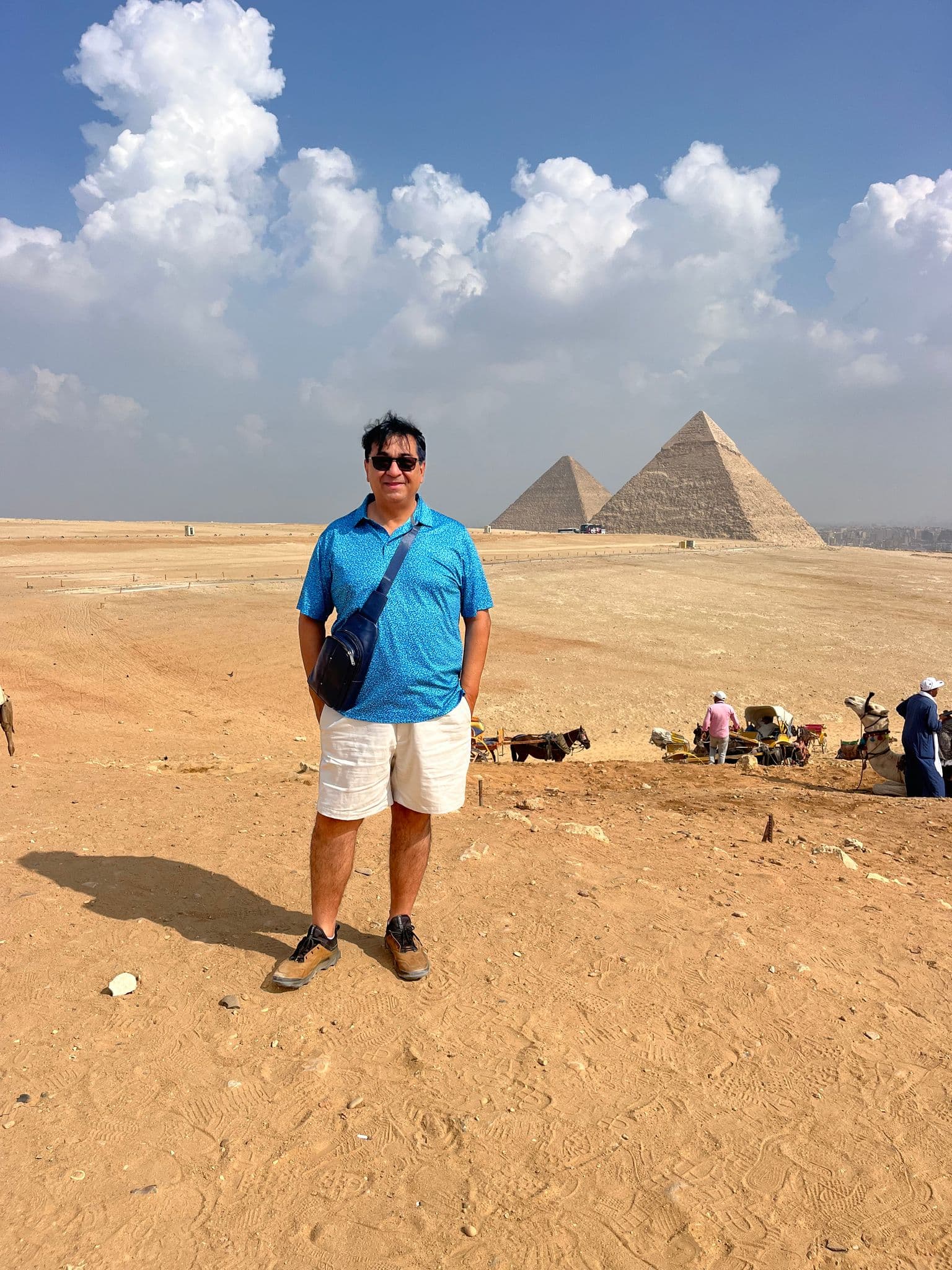 Pyramids of Giza behind a tourist standing on the desert with camels and handlers visible on the horizon, Giza, Egypt