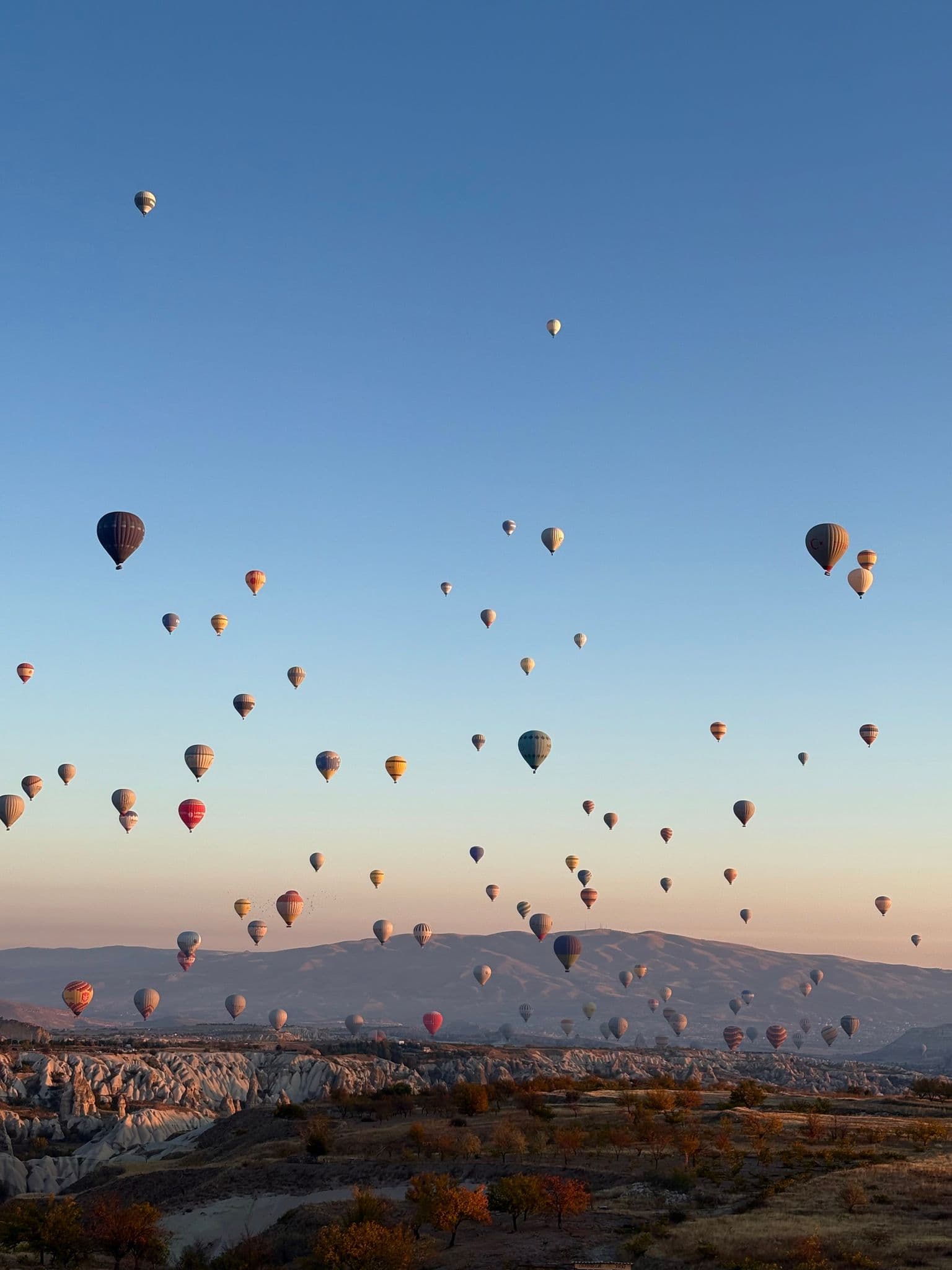 Hot air balloons filling the sky over Love Valley in Cappadocia, Turkey, with Mount Erciyes on the distant horizon.