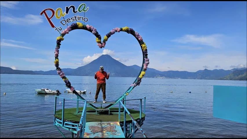 Heart-shaped floral frame on a pier at Lake Atitlán in Panajachel, Guatemala, with Volcán San Pedro behind and a person standing on the platform