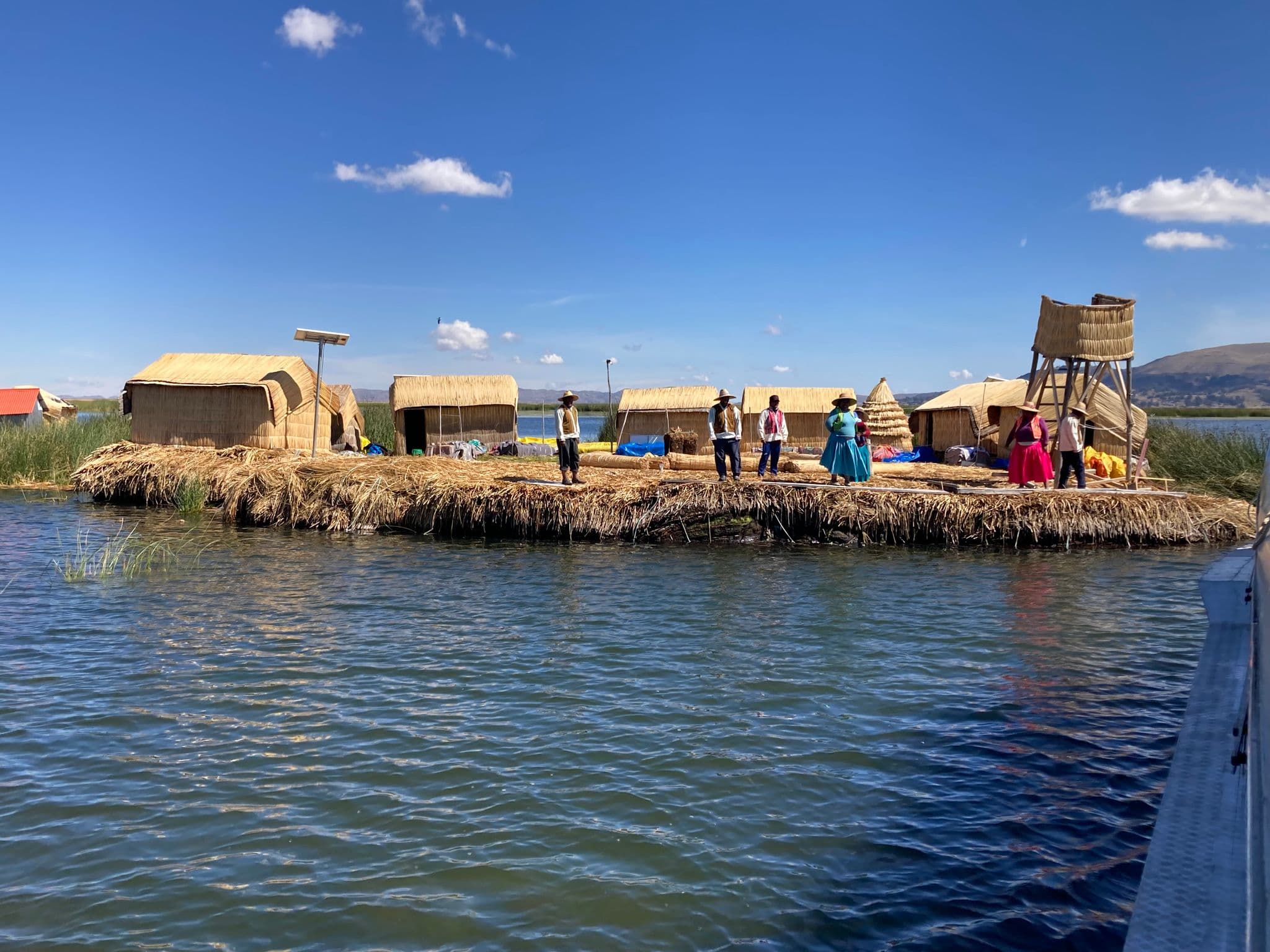 Uros floating island on Lake Titicaca with reed huts and local people standing on the shore, Peru.