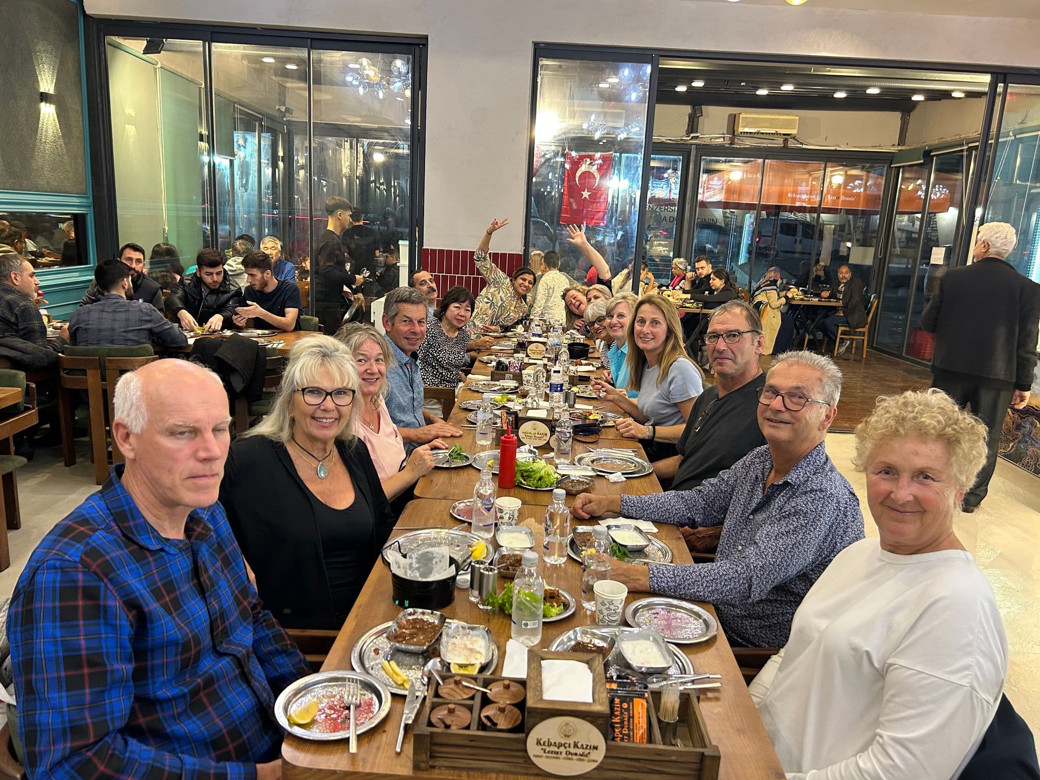 Group of people dining at a long restaurant table with a Turkish flag visible through the windows in Istanbul, Turkey.