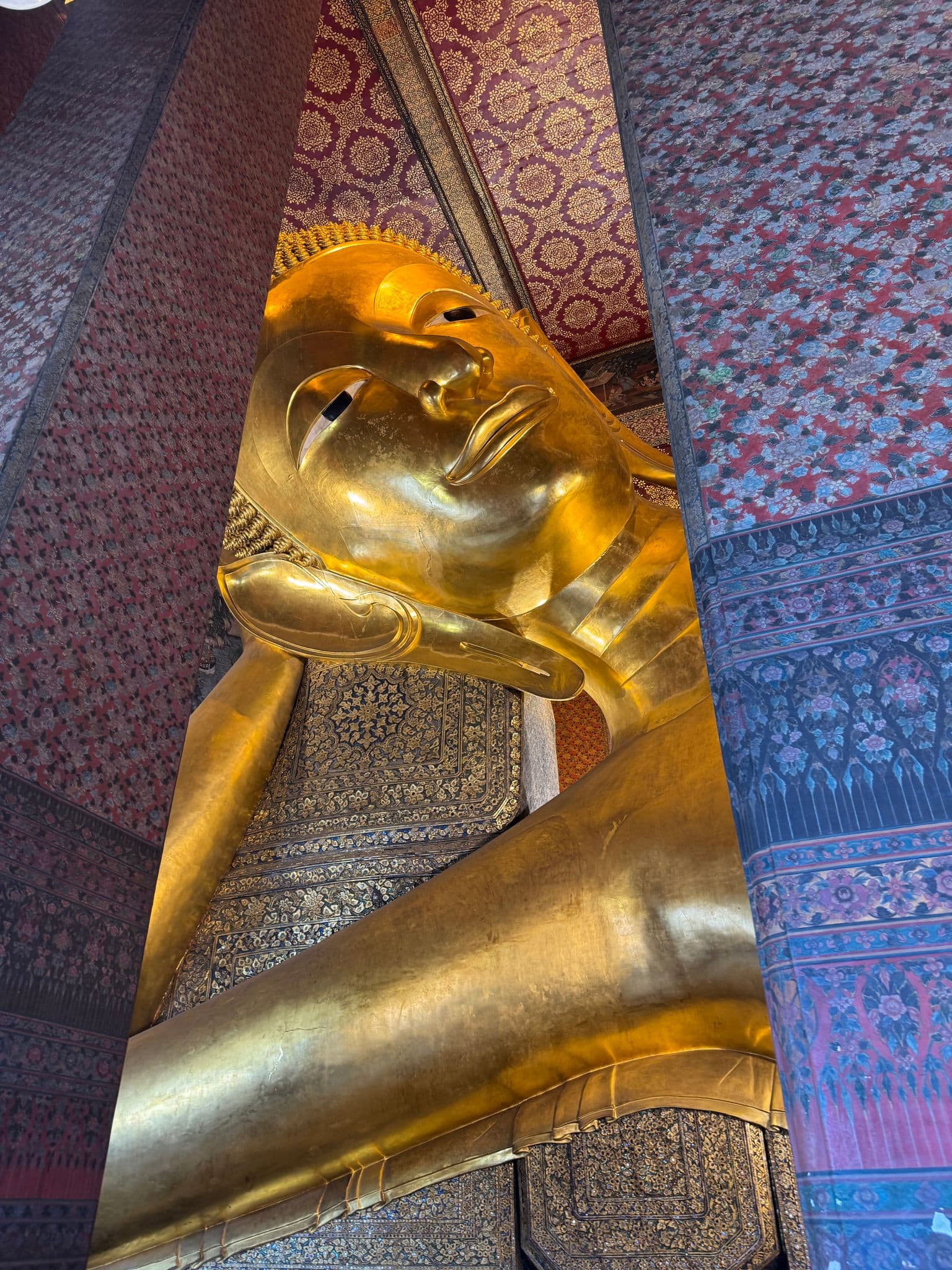 Reclining Buddha statue at Wat Pho in Bangkok, Thailand, shown from the side inside an ornate temple interior