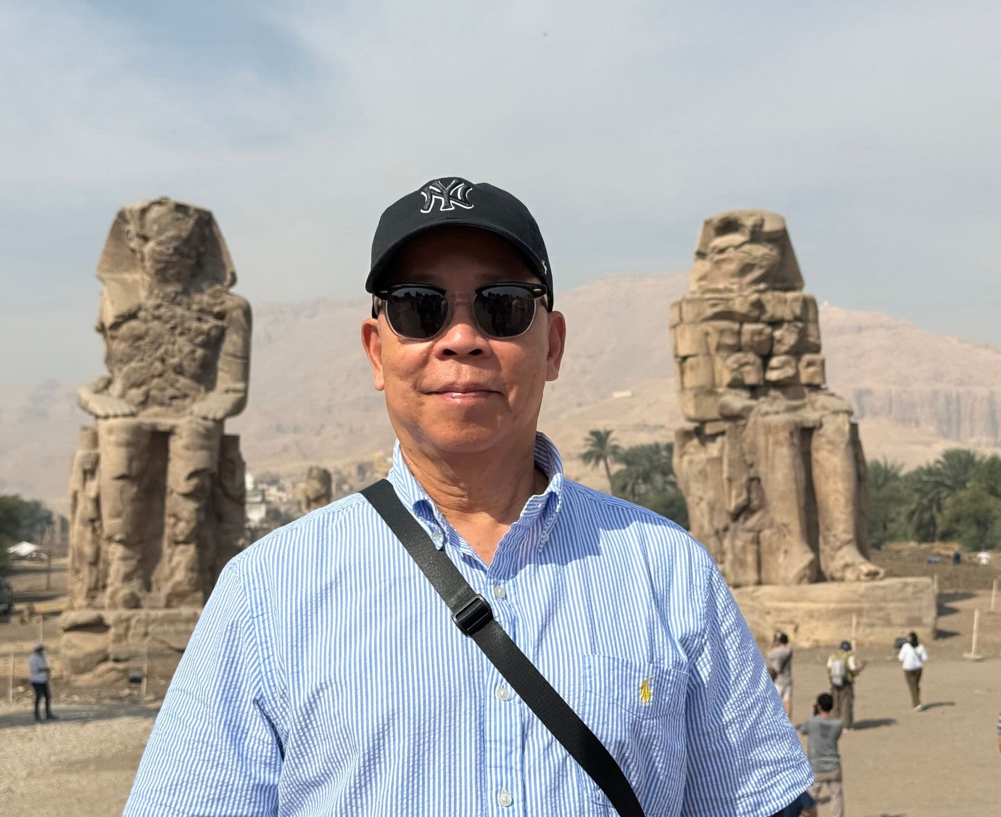 Colossi of Memnon behind a man wearing a cap and sunglasses, West Bank, Luxor, Egypt.