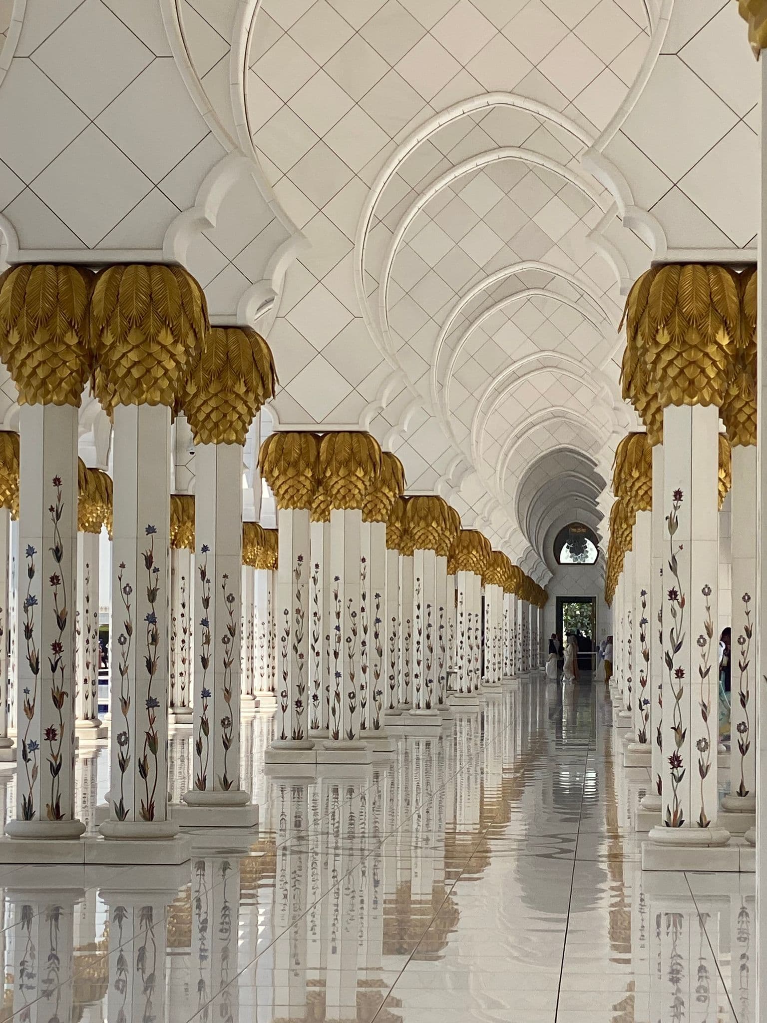 Gold-capped columns of Sheikh Zayed Grand Mosque reflected on a polished marble floor, Abu Dhabi, United Arab Emirates.