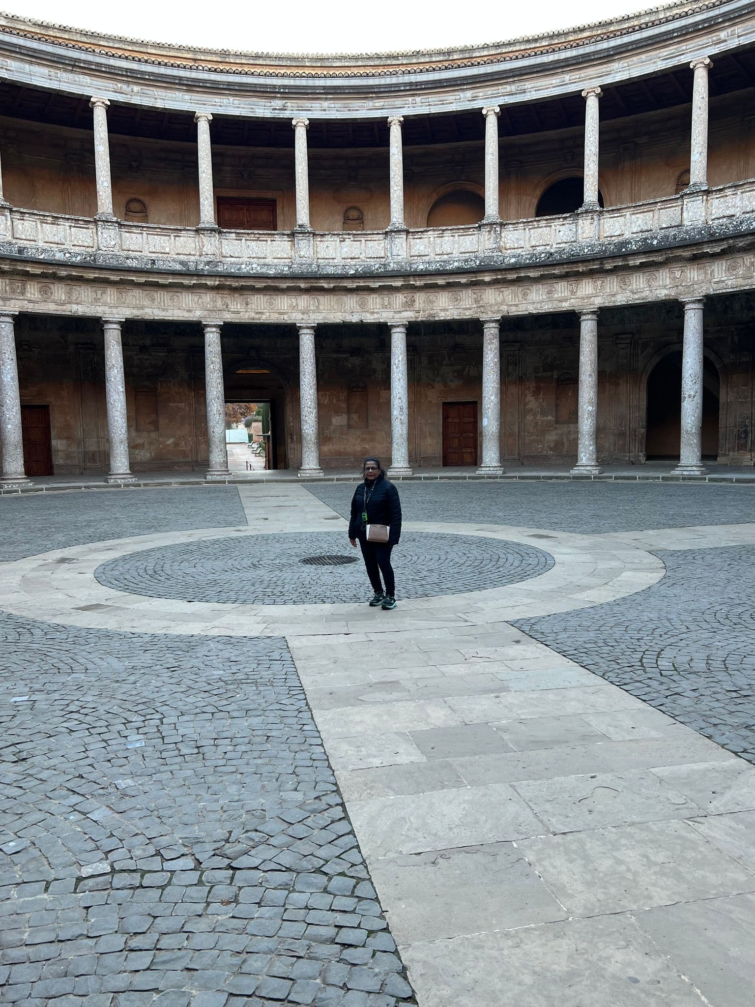 Circular Renaissance courtyard of the Palace of Charles V at the Alhambra in Granada, Spain, with a traveler standing near the center