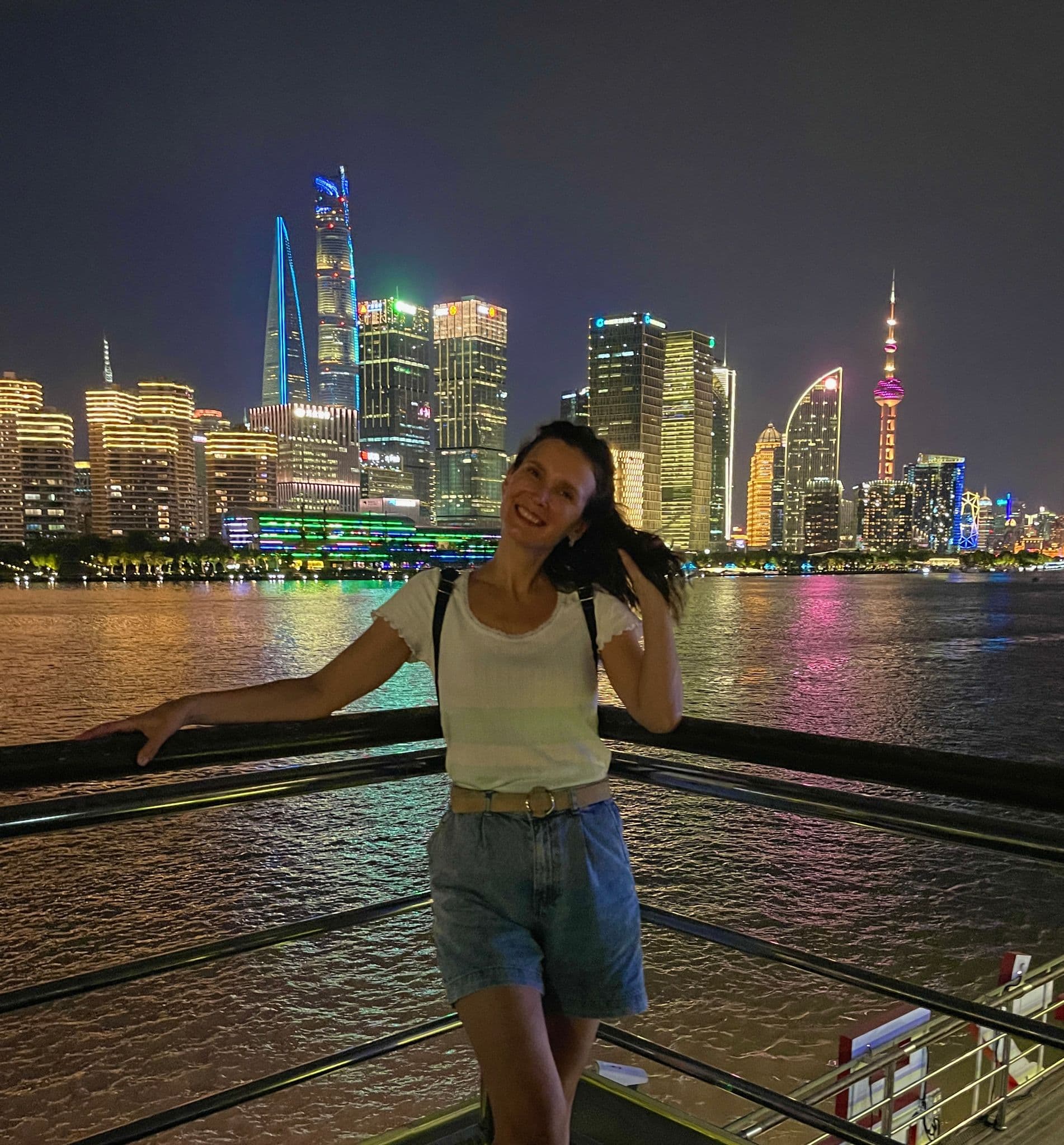 Oriental Pearl Tower and Shanghai skyline at night over the Huangpu River, with a traveler leaning on a railing in Shanghai, China.