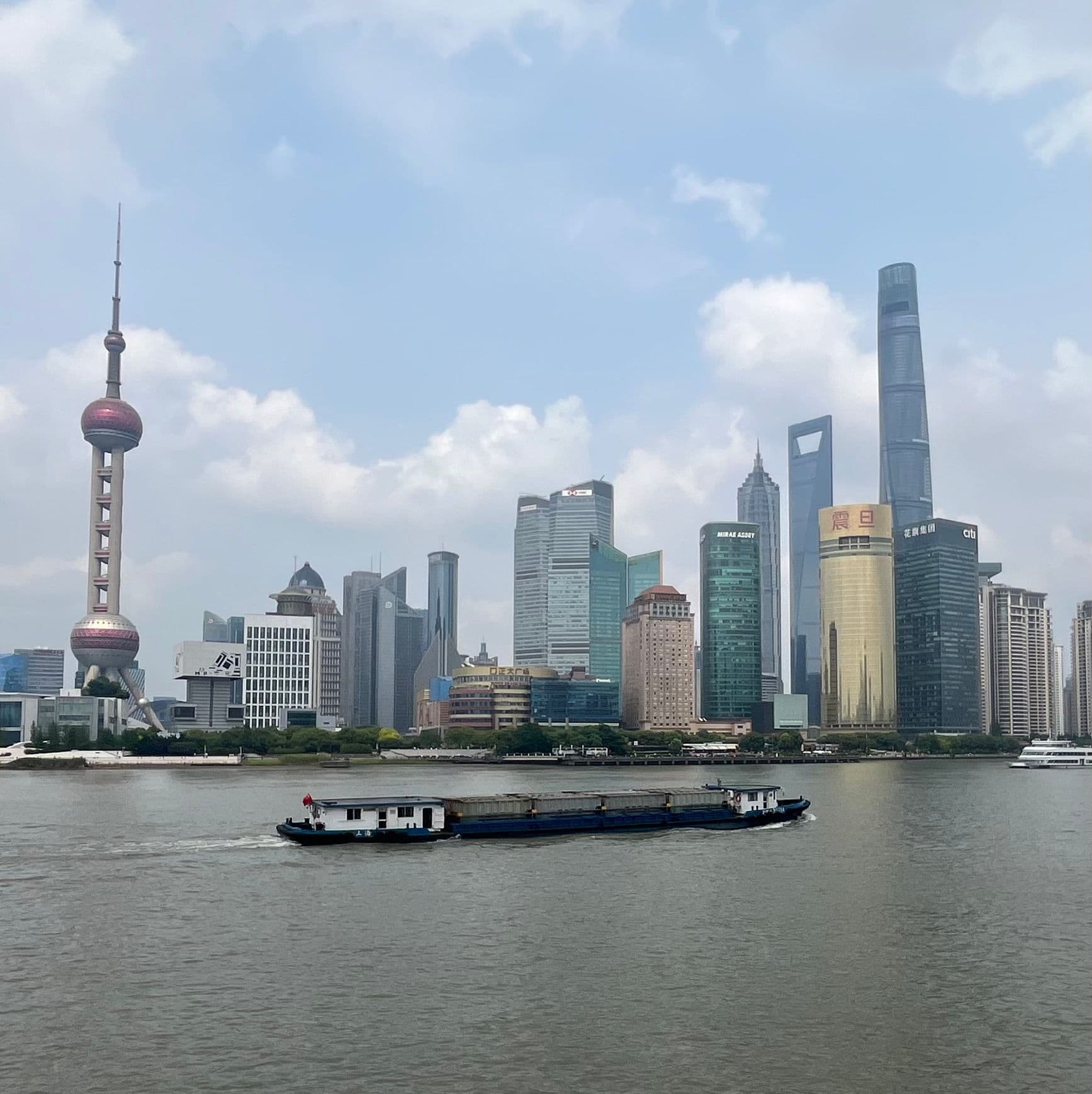 Oriental Pearl Tower and the Lujiazui skyline across the Huangpu River with a cargo boat passing, The Bund, Shanghai, China.