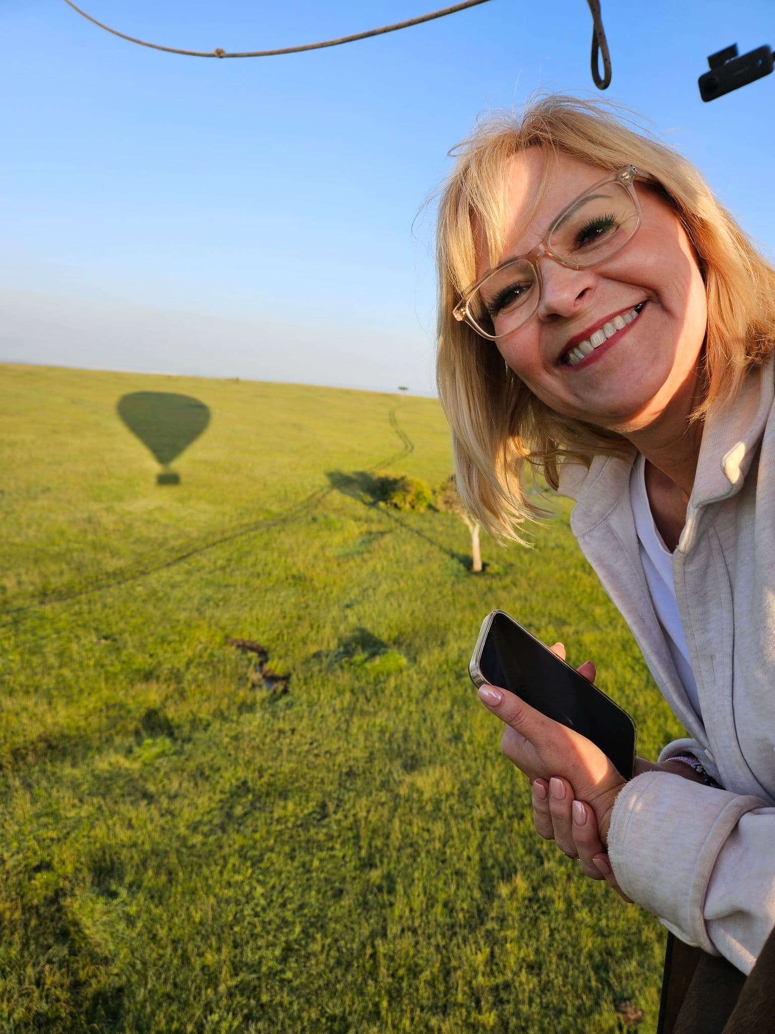Woman leaning from a hot air balloon basket over the grassy plains of Masai Mara National Reserve, Kenya.