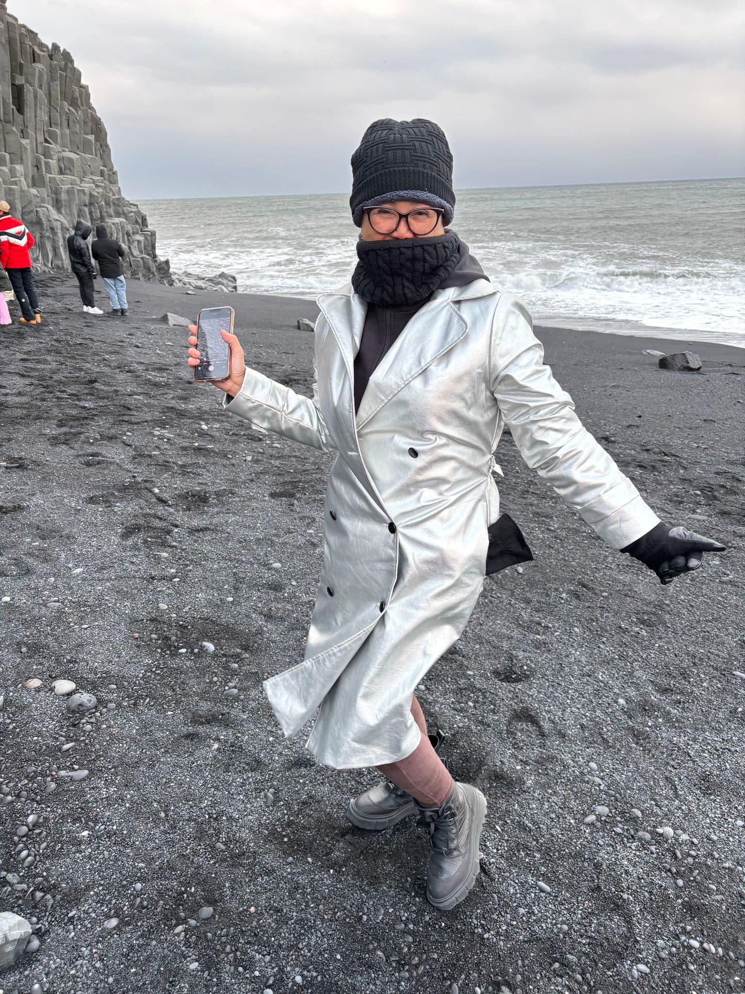 Reynisfjara Black Sand Beach with a bundled traveler posing on the black sand shore, basalt columns and waves in Vík, Iceland.