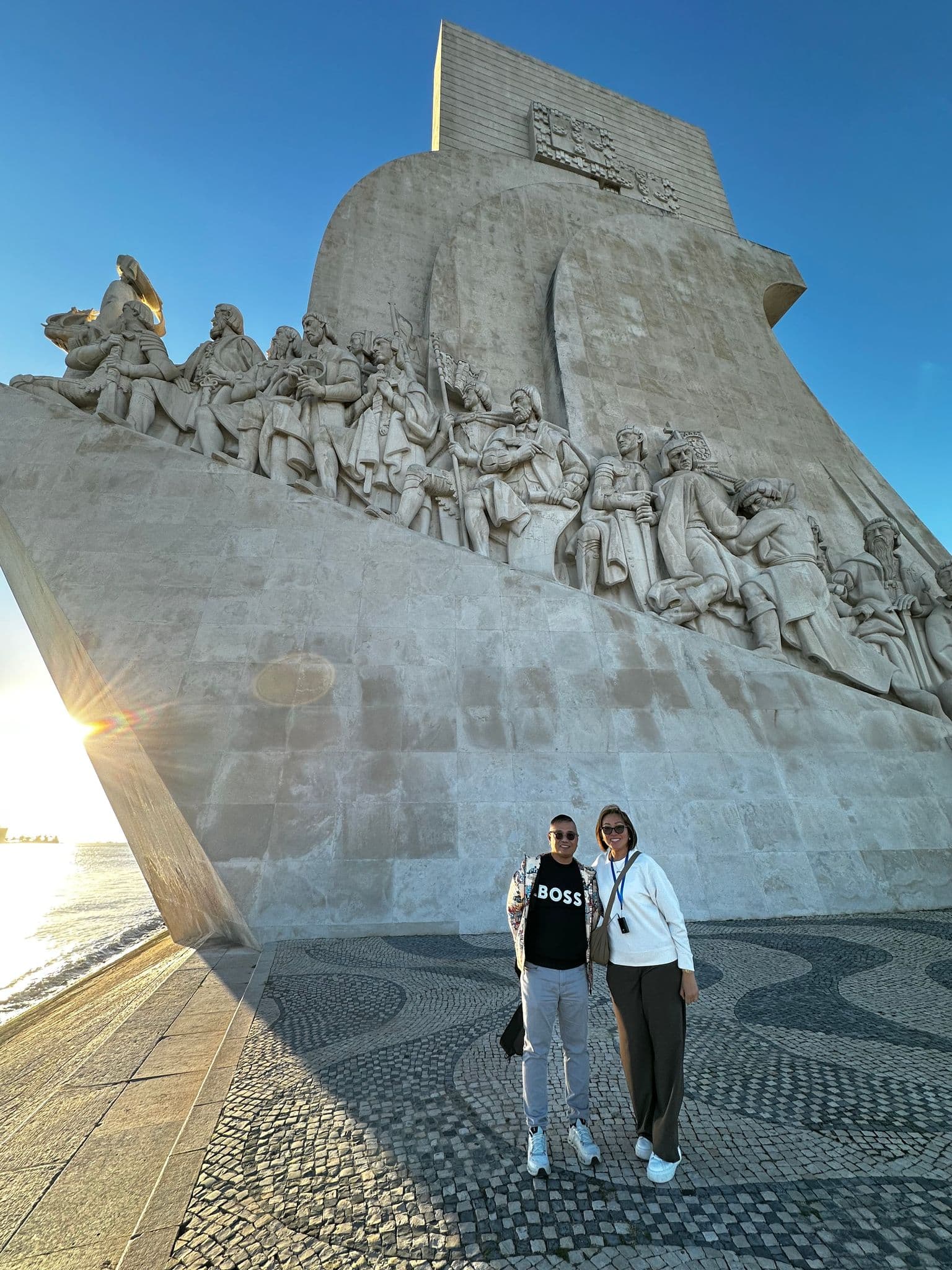 Padrão dos Descobrimentos monument in Lisbon with two people posing on the Tagus riverfront at sunset, Portugal.