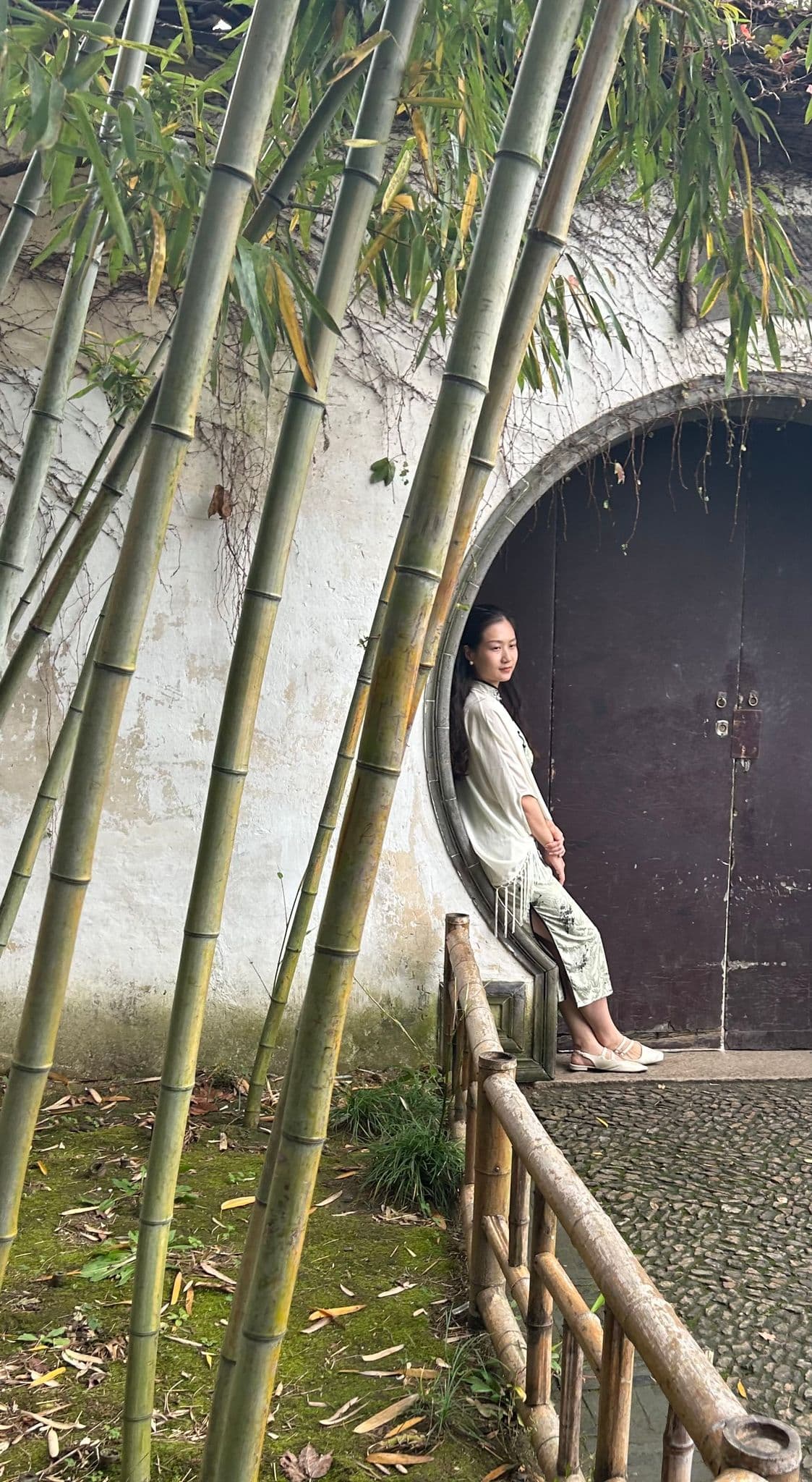 Moon gate at the Lingering Garden in Suzhou, China, with a woman leaning in the circular doorway beside bamboo