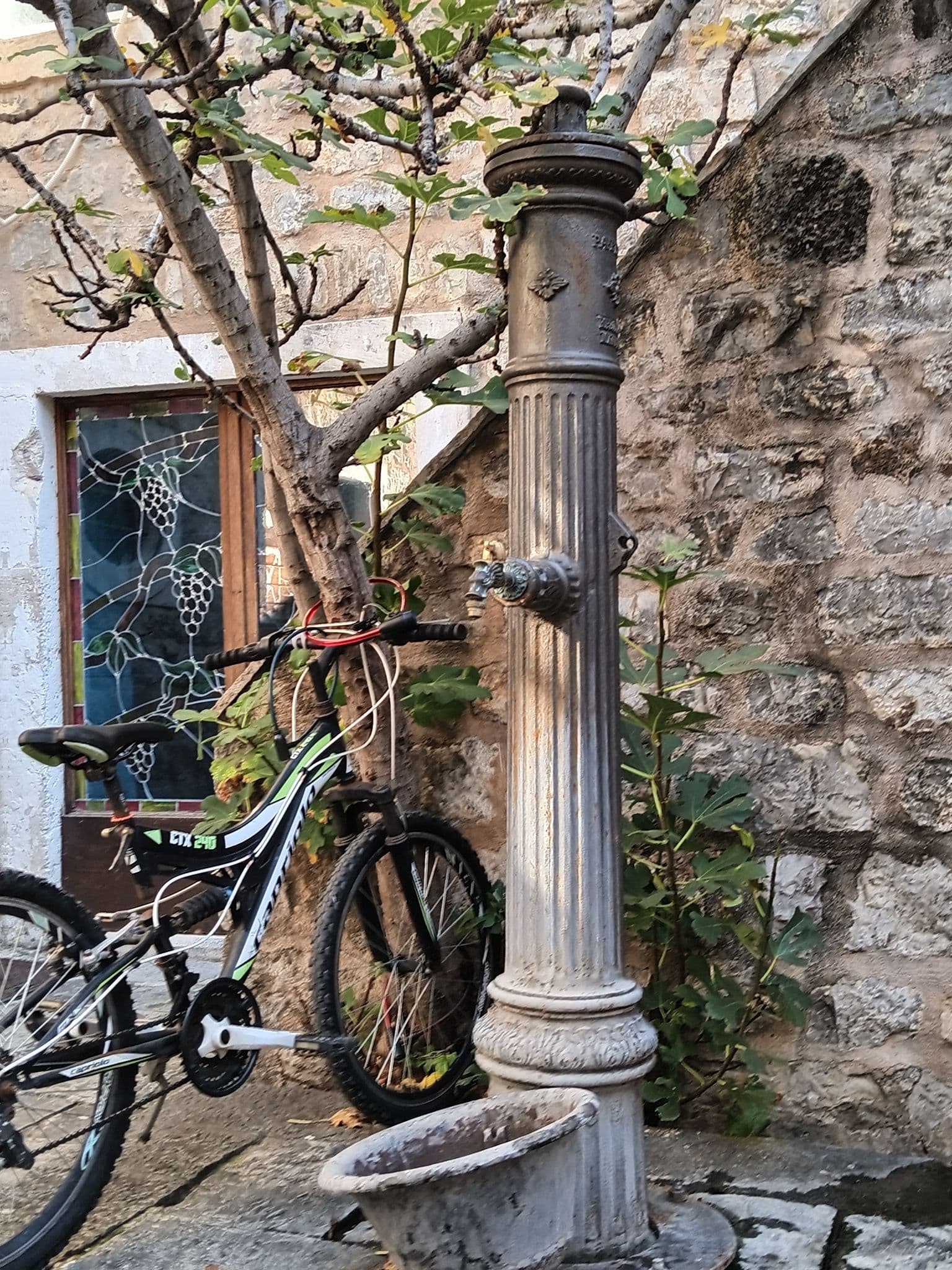 Cast-iron street water fountain next to a parked bicycle against a stone wall in a narrow alley.