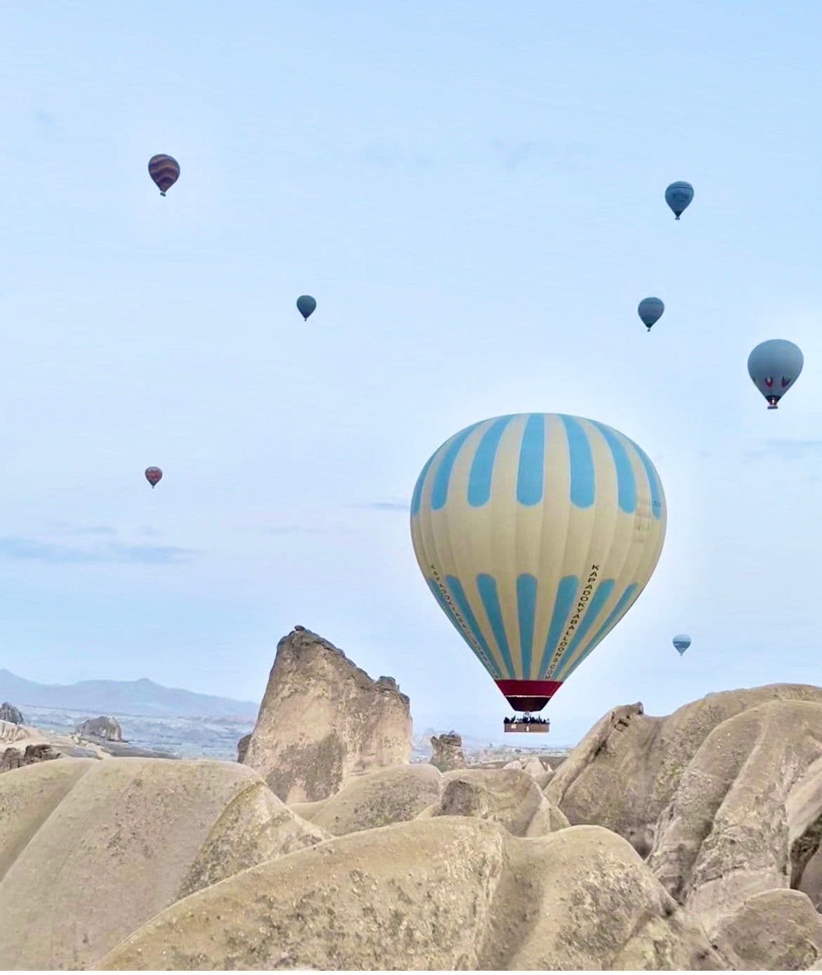Striped hot air balloon floating above Cappadocia's rock formations and fairy chimneys, with other balloons in the sky, Turkey.