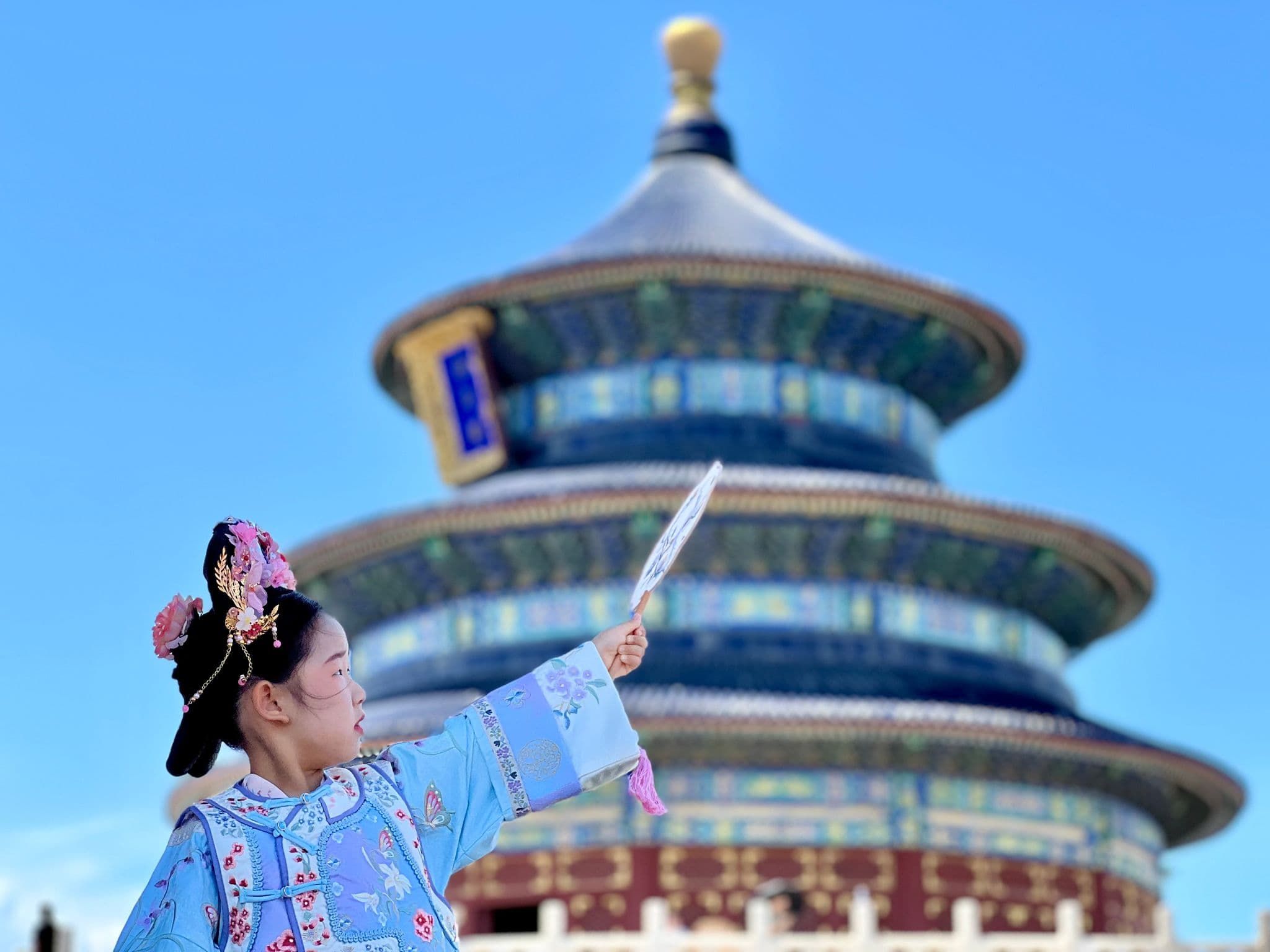 Temple of Heaven in Beijing with a girl in traditional dress holding a fan in the foreground during a photoshoot