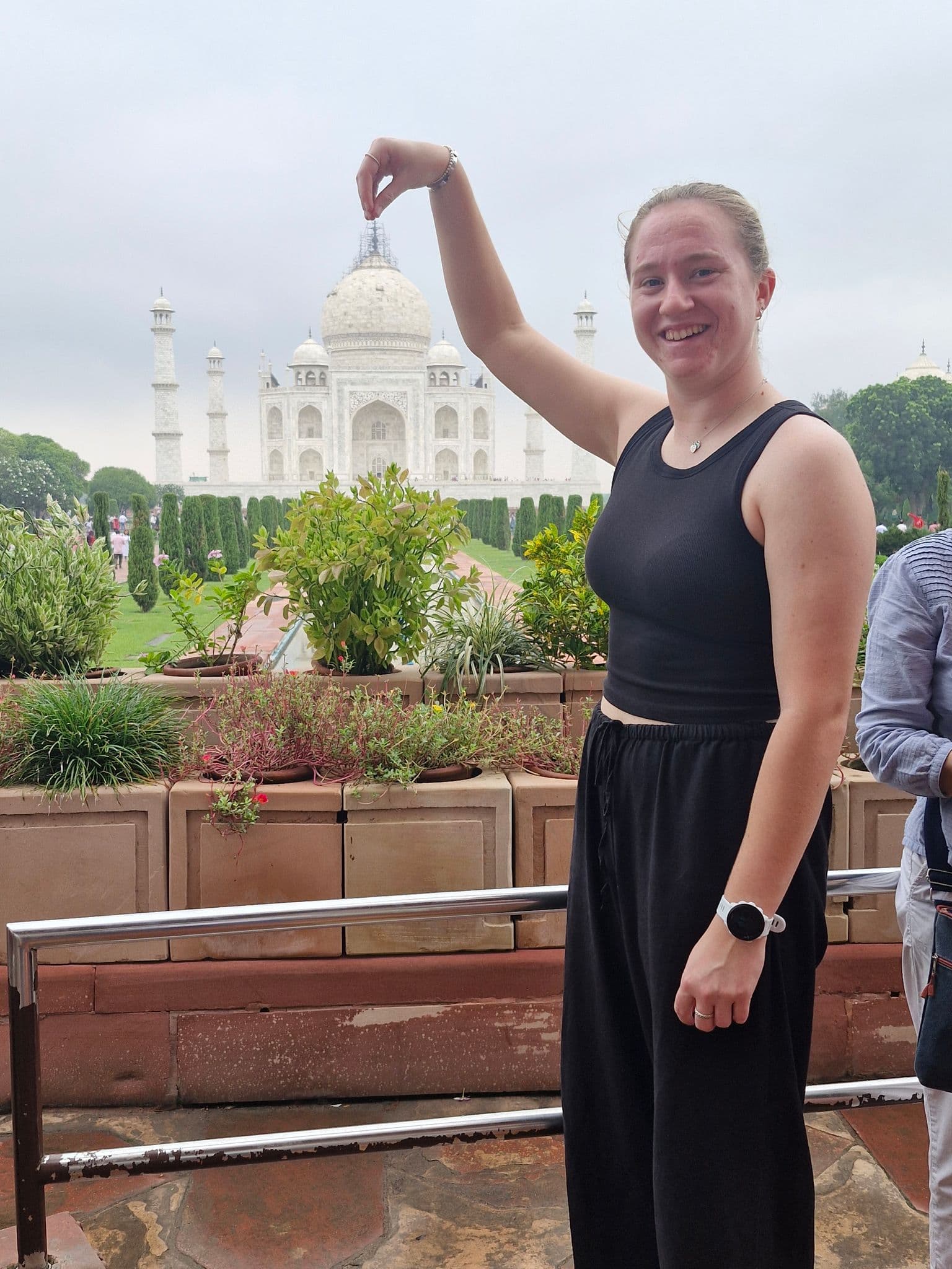 Taj Mahal in Agra, India with a woman posing to pinch the dome from a garden viewing area.