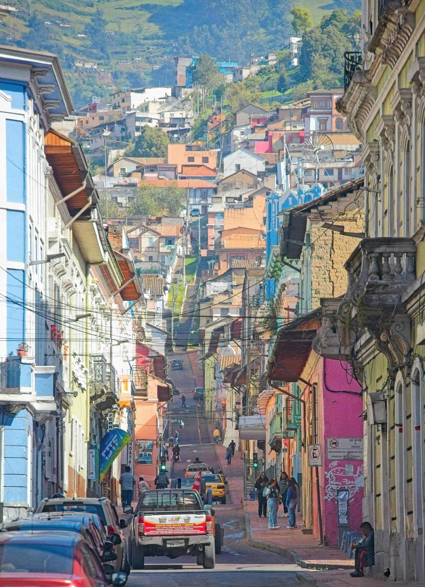 Colorful steep street in Quito's Historic Center with people walking and cars driving up the hill, Ecuador.