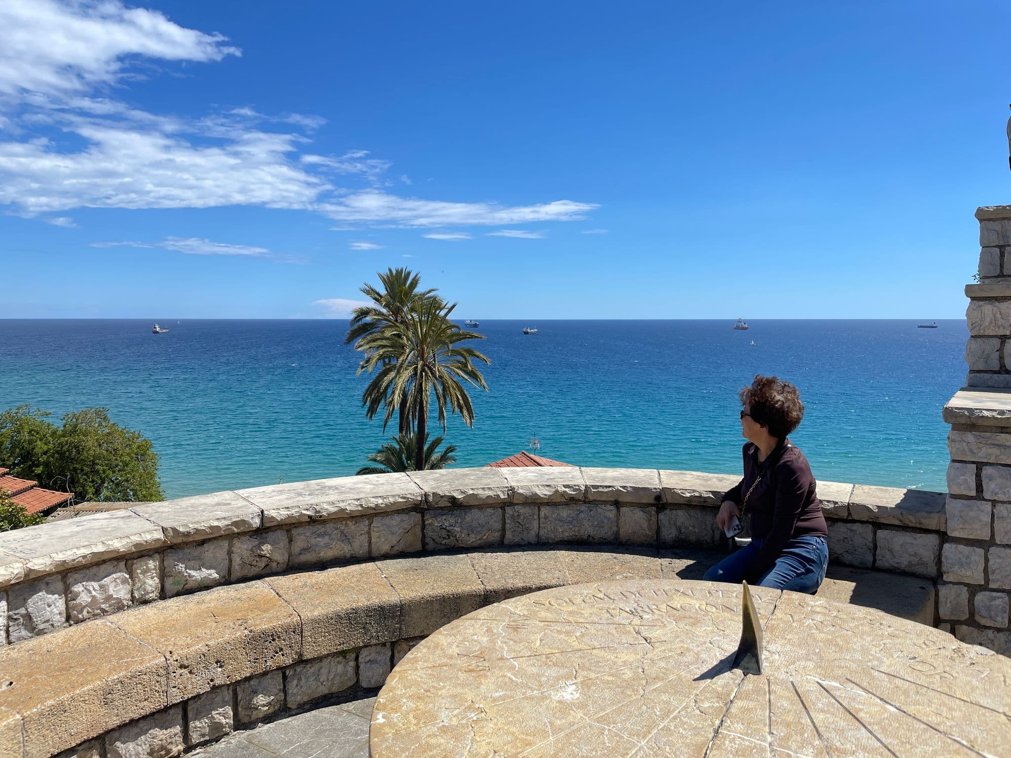 Balcony of the Mediterranean viewpoint in Tarragona, Spain, showing a person seated on a stone bench looking out toward the sea and a palm tree.