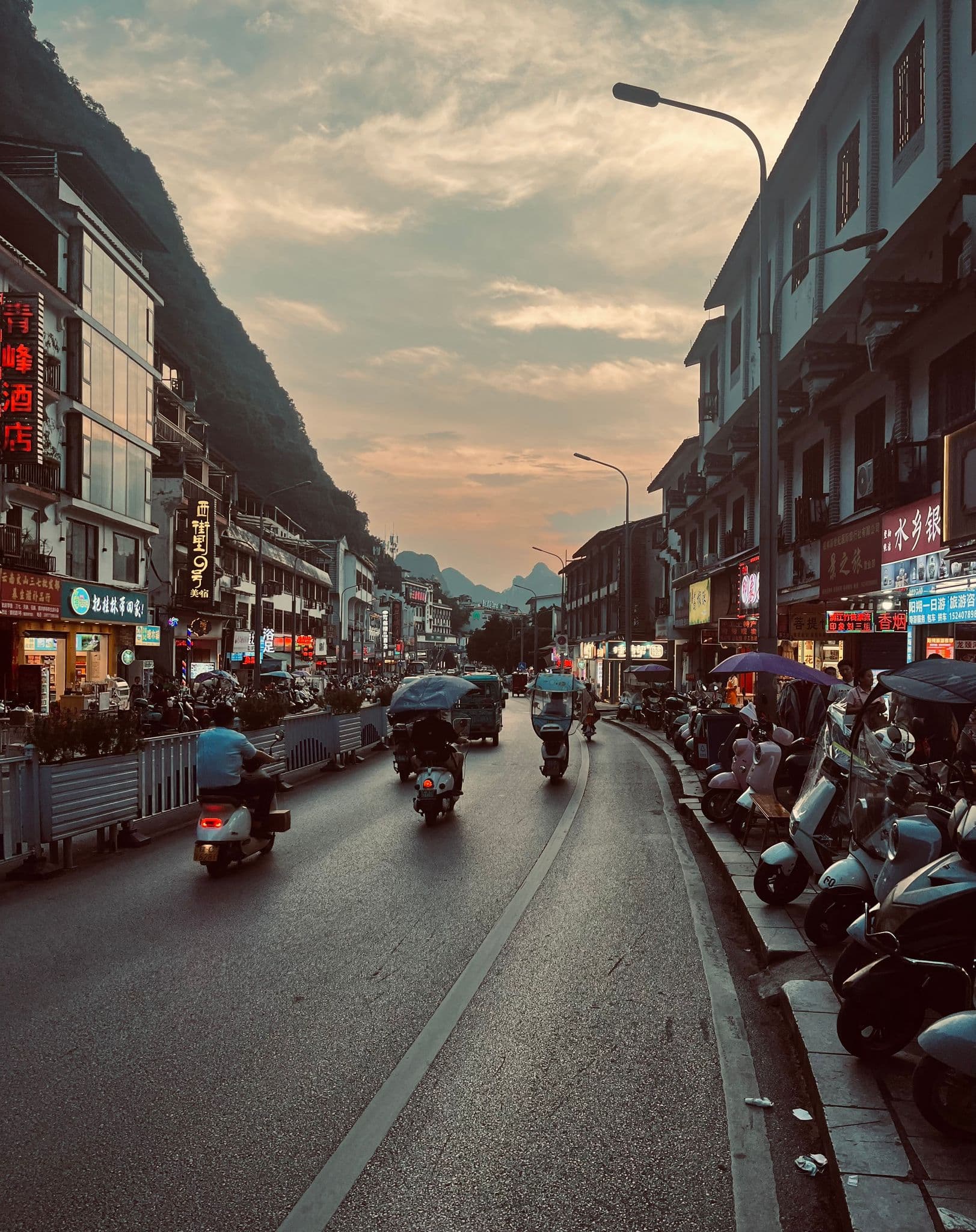 Karst peaks near Yangshuo framed over a busy street where scooters travel at sunset, Yangshuo, Guangxi, China.