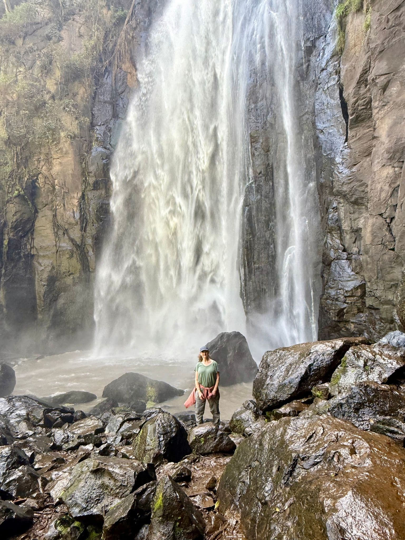 Thomson's Falls (Nyahururu Falls) cascading down a rocky cliff with a person standing on wet boulders at the base, Nyahururu, Kenya