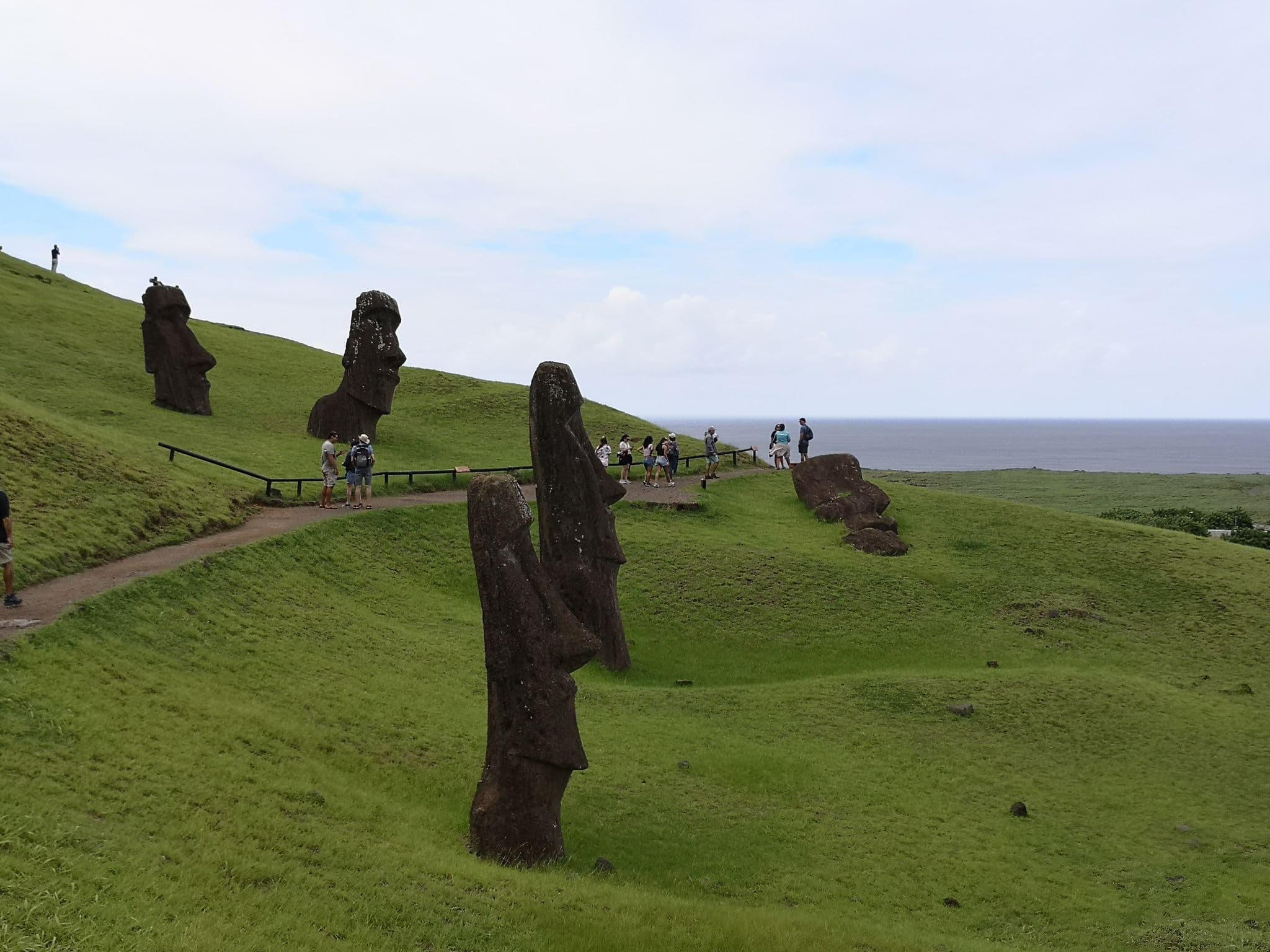 Moai statues at Rano Raraku quarry on Rapa Nui (Easter Island), Chile, on a grassy slope with tourists viewing the site.