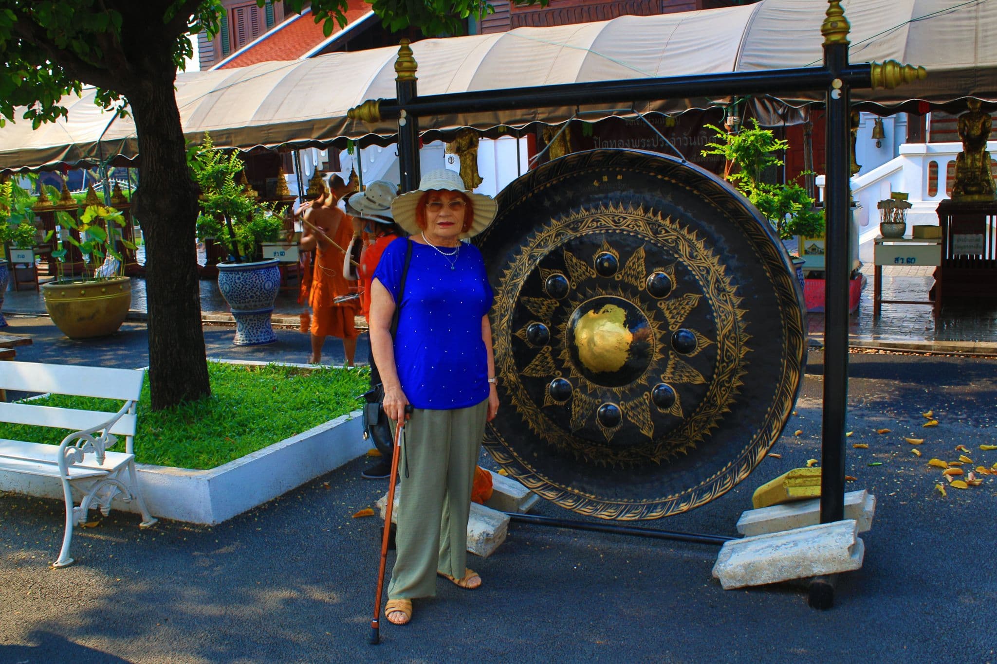 Large ornate gong with a golden center beside a woman standing with a cane at a Buddhist temple in Bangkok, Thailand.