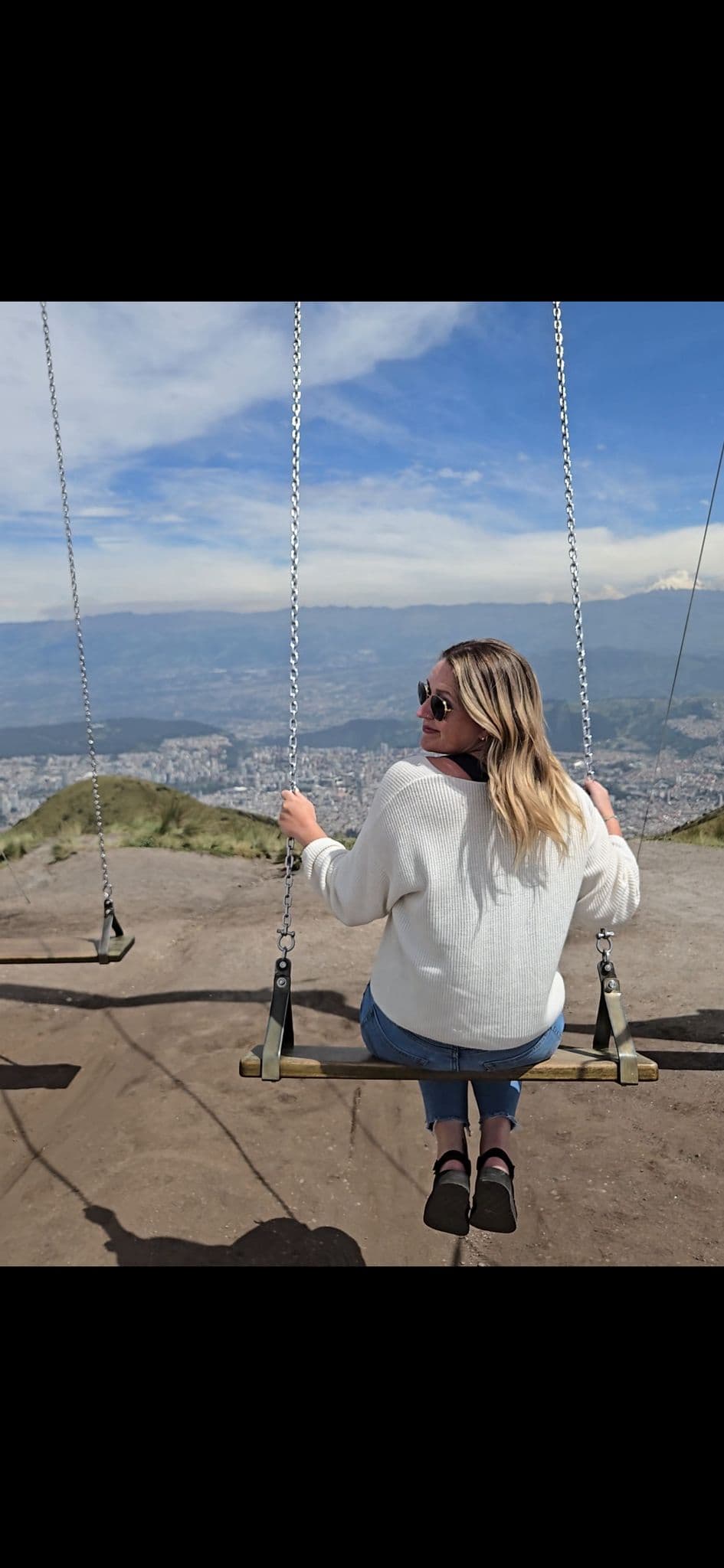 Person on a swing at the TelefériQo/Cruz Loma viewpoint overlooking Quito, Ecuador, with mountains and the city below.
