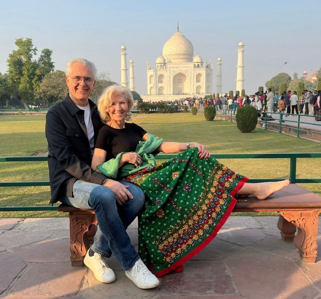 Taj Mahal in Agra, India with a couple sitting on a bench in the foreground and the mausoleum visible behind them.