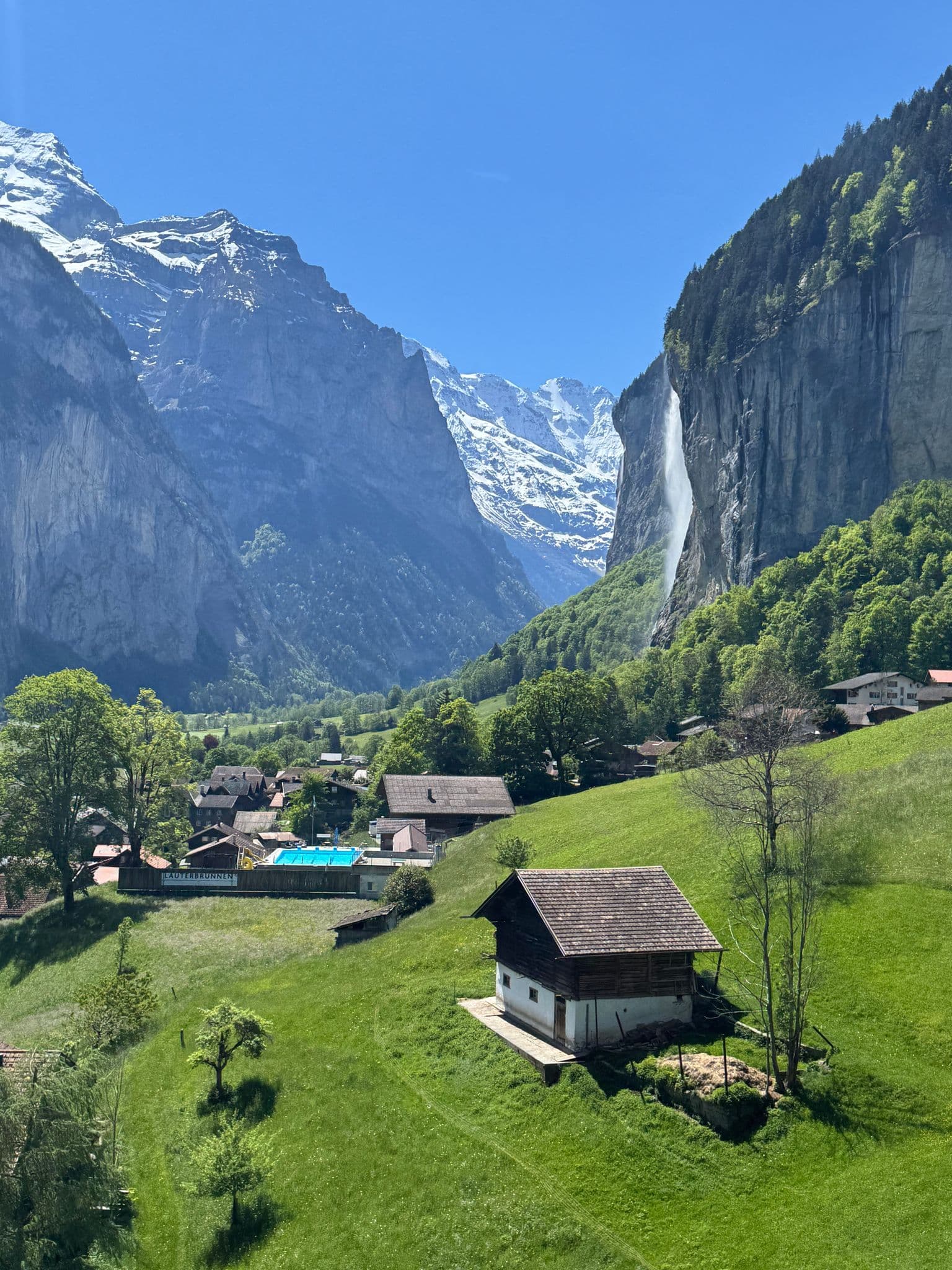 Staubbach Falls plunging down a cliff beside chalets and a green meadow in Lauterbrunnen Valley, Switzerland.