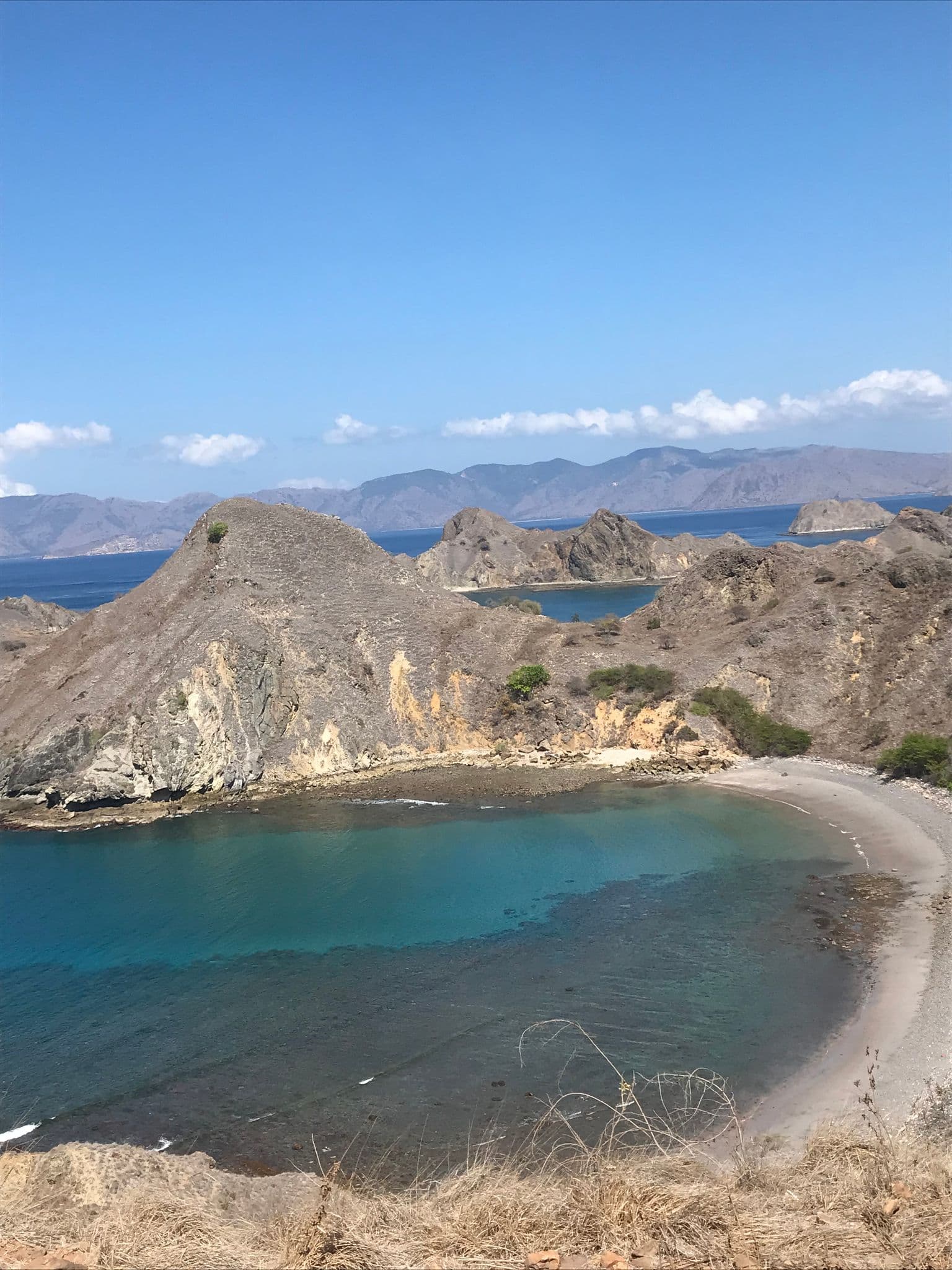 Padar Island viewpoint overlooking a curved turquoise bay and rocky, dry hills in the Komodo Islands, Indonesia.