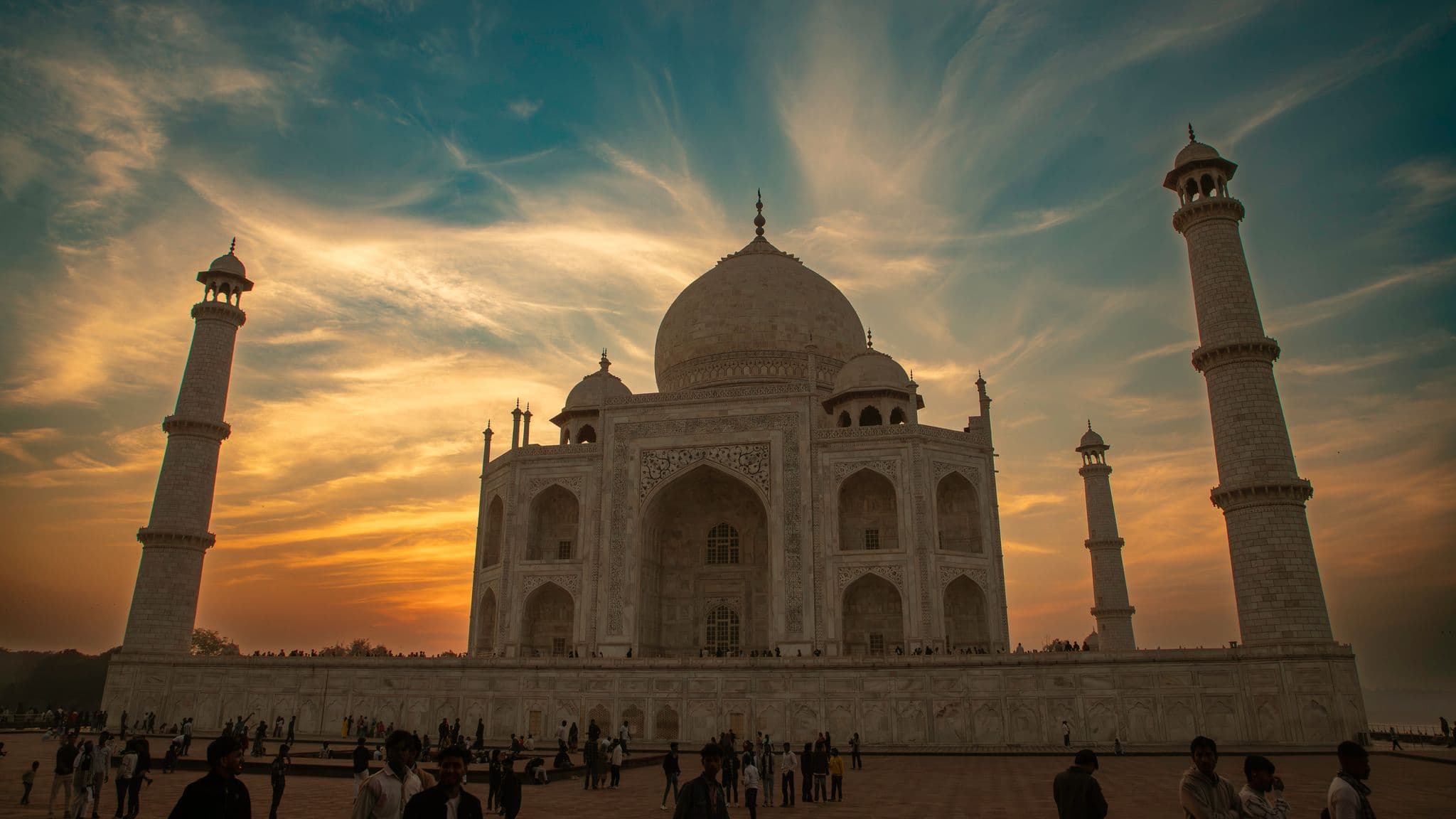 Taj Mahal at sunset with visitors gathered on the forecourt in Agra, India.