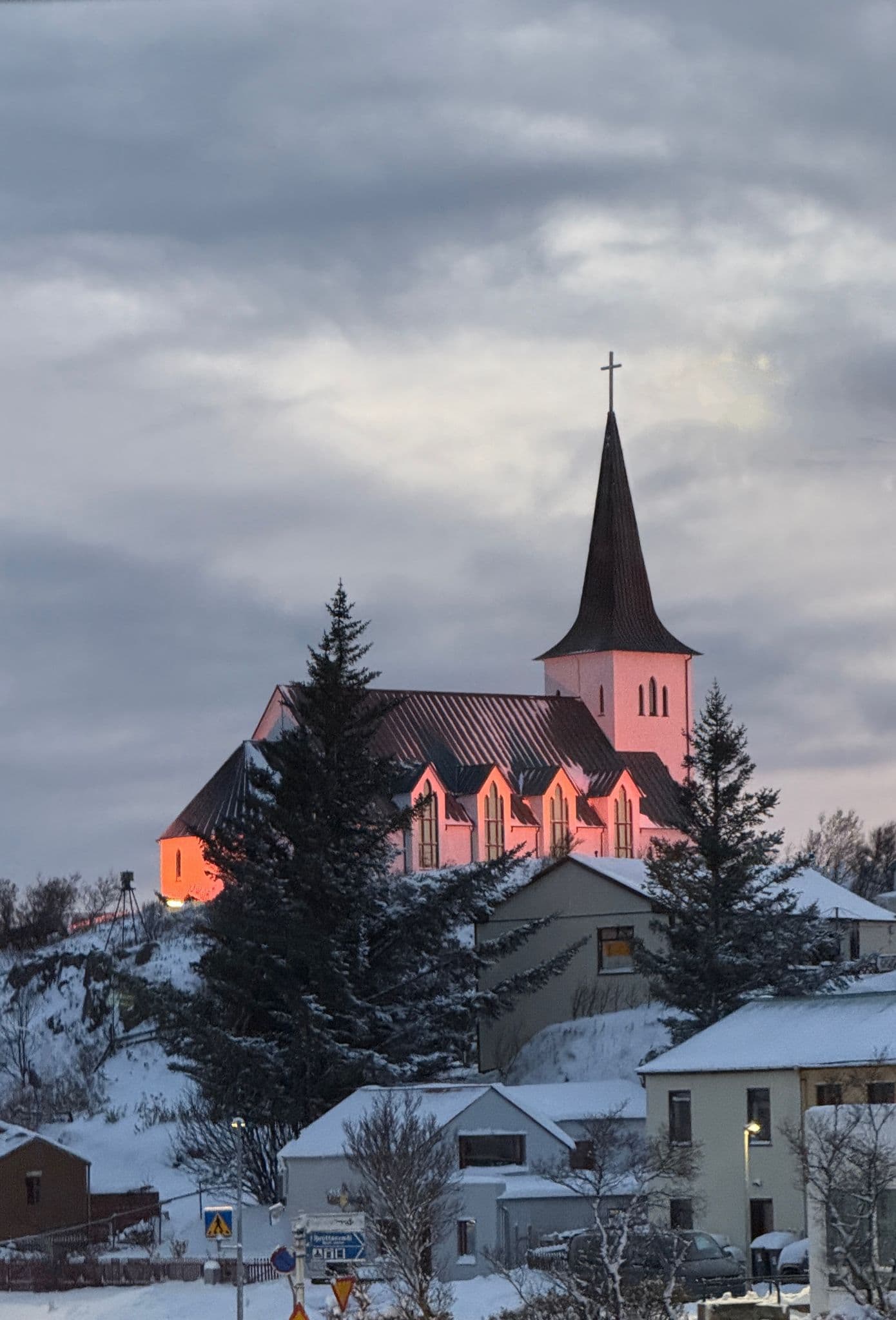 Hilltop church with a tall spire lit by pink evening light above snowy houses in Iceland.