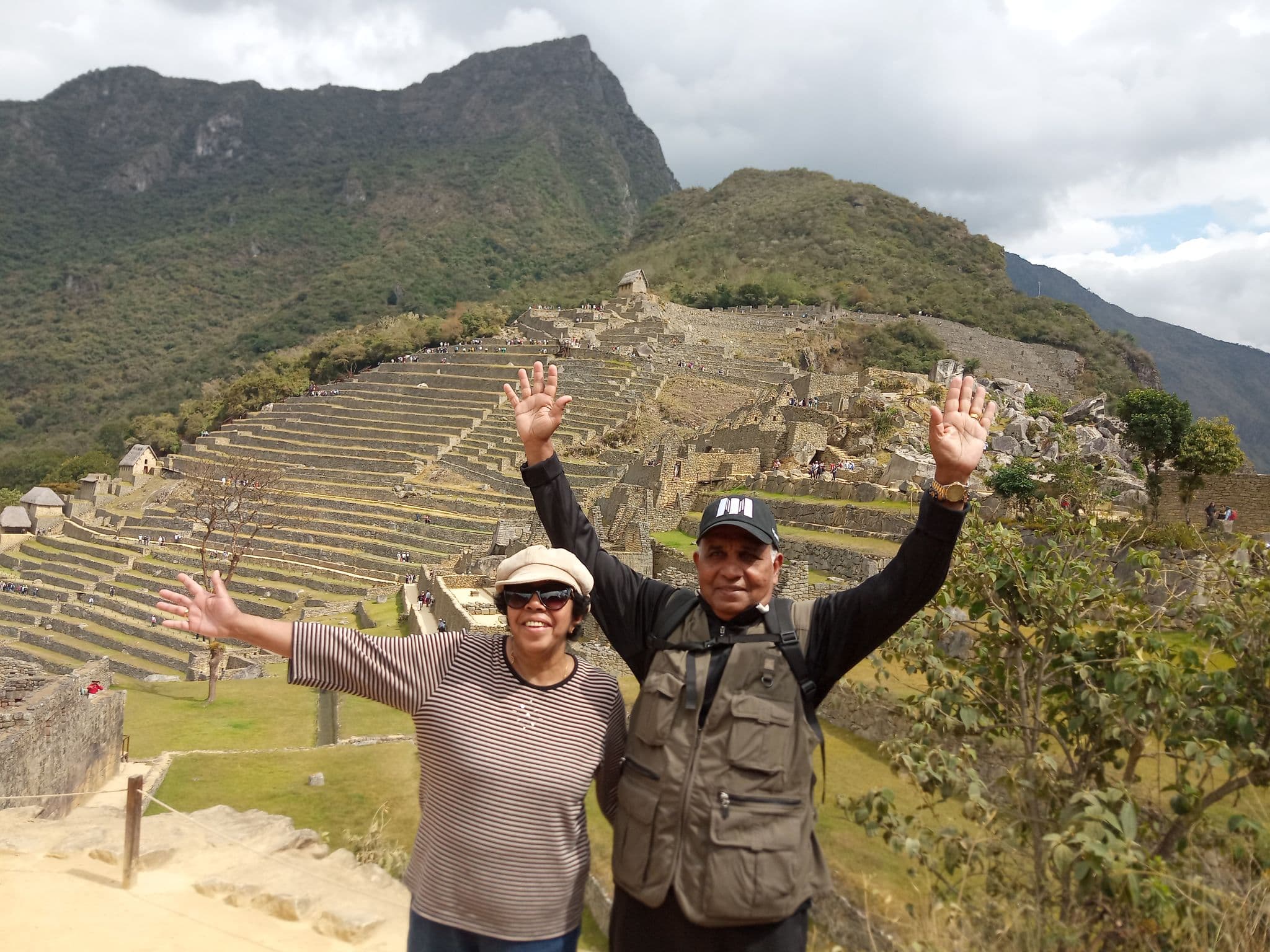 Machu Picchu terraces with two travelers raising their arms on a path, Cusco Region, Peru.