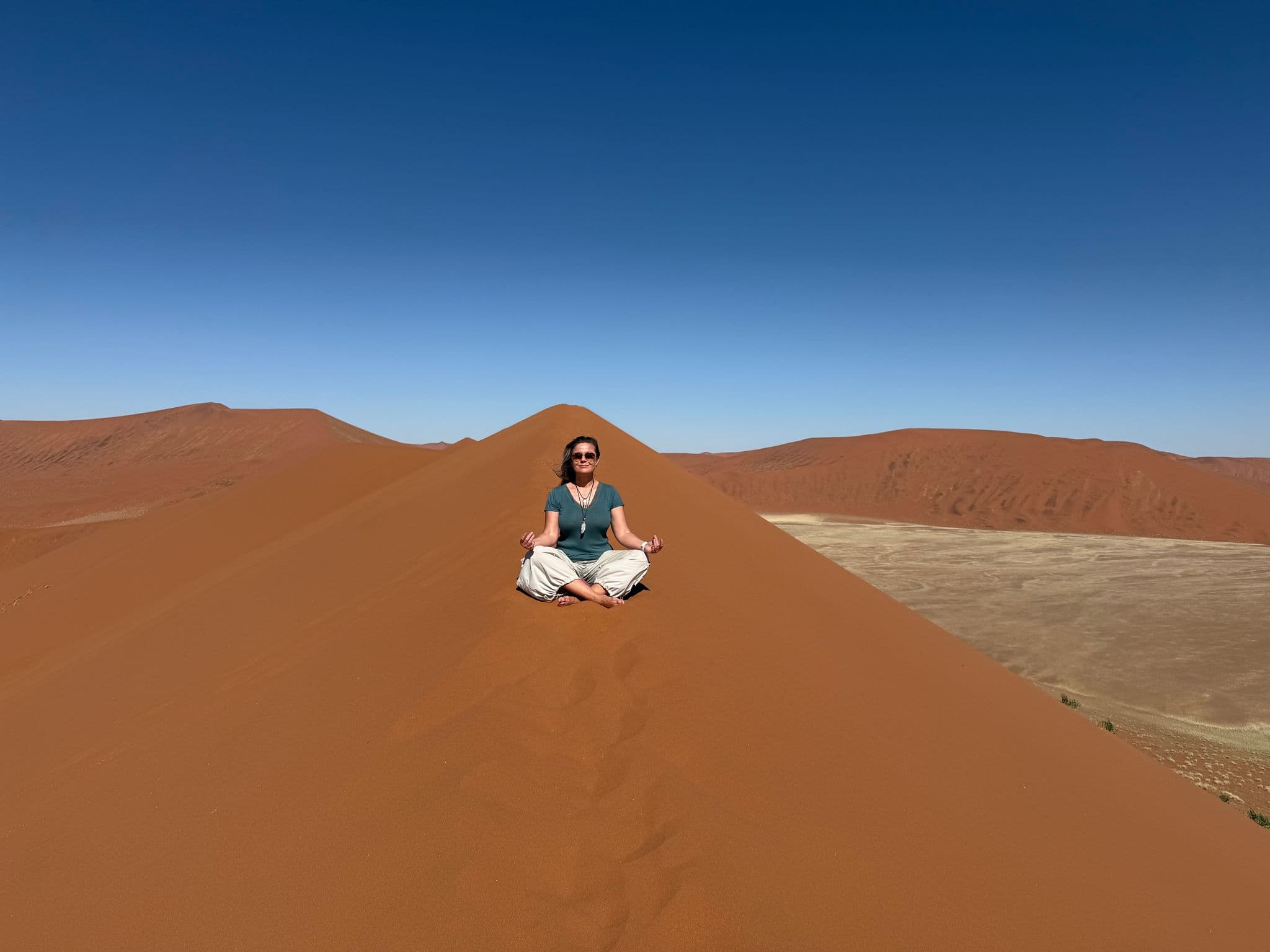 Sand dune ridge at Sossusvlei in the Namib Desert, Namibia, with a person sitting cross-legged on the crest.