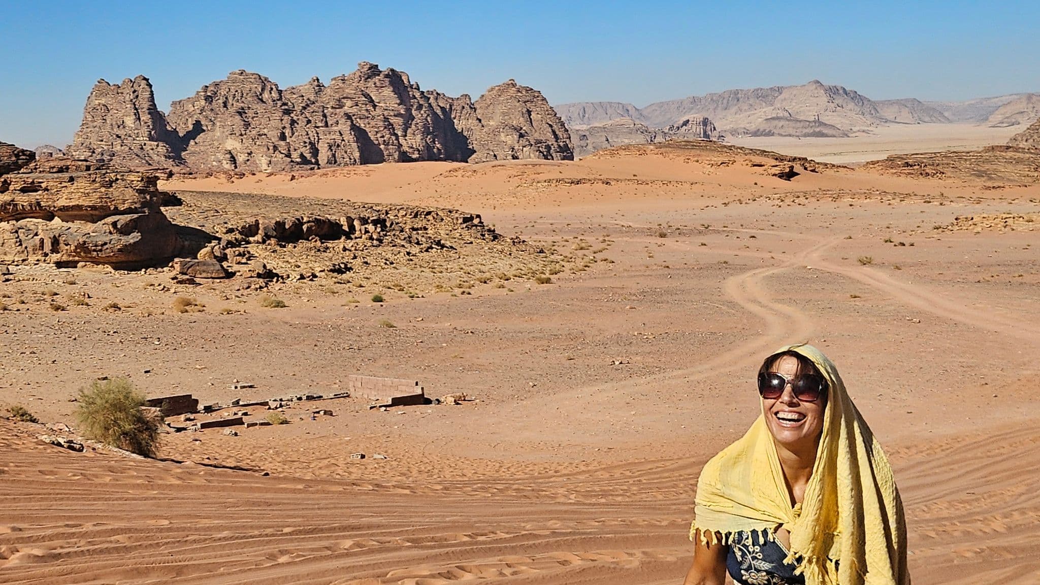 Wadi Rum sandstone rock formations with a smiling traveler in a yellow headscarf standing on rippled sand dunes, Jordan.